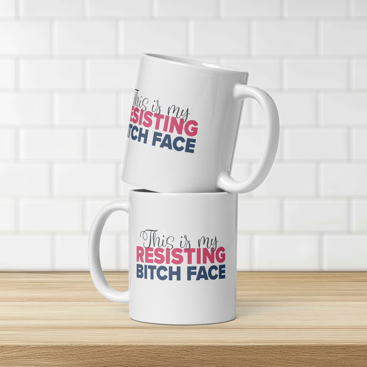 Two stacked glossy white ceramic coffee mugs with a graphic that reads "This is my resisting bitch face" in stylized text, showing that the same graphic is on both sides of the cup.