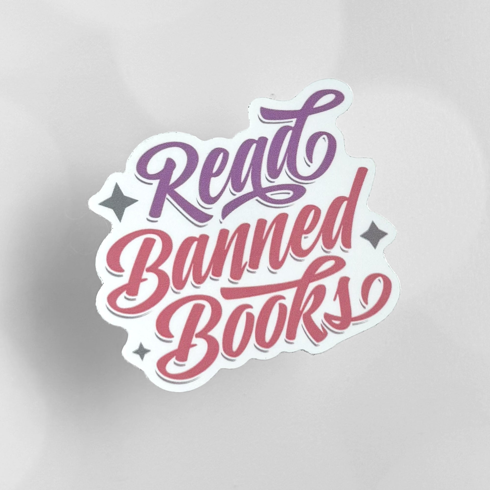 Retro-style "Read Banned Books" die-cut vinyl sticker with purple and pink script lettering.