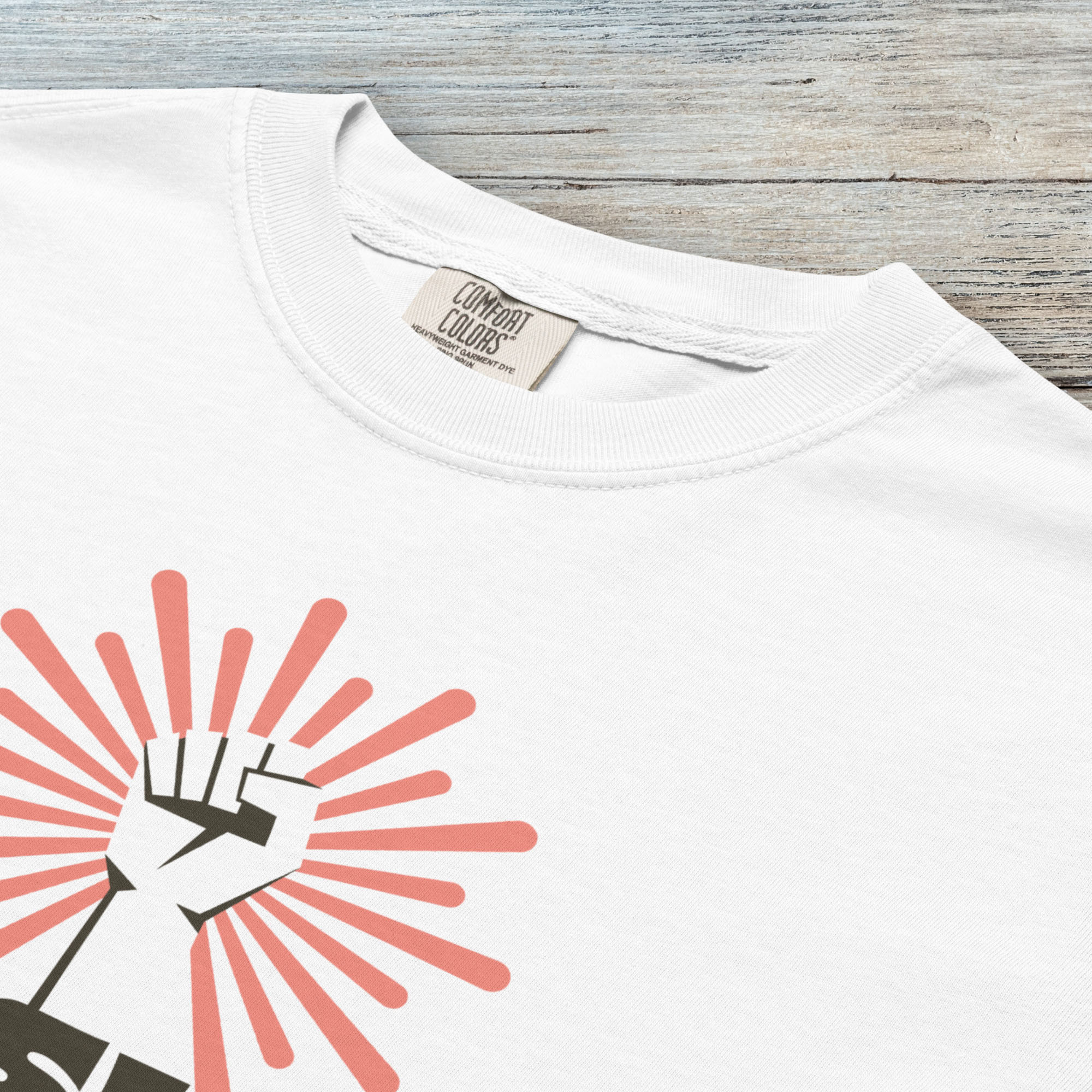 Closeup detail of white t-shirt with retro style "resist" text, raised fist, and pinkish burst behind the fist.
