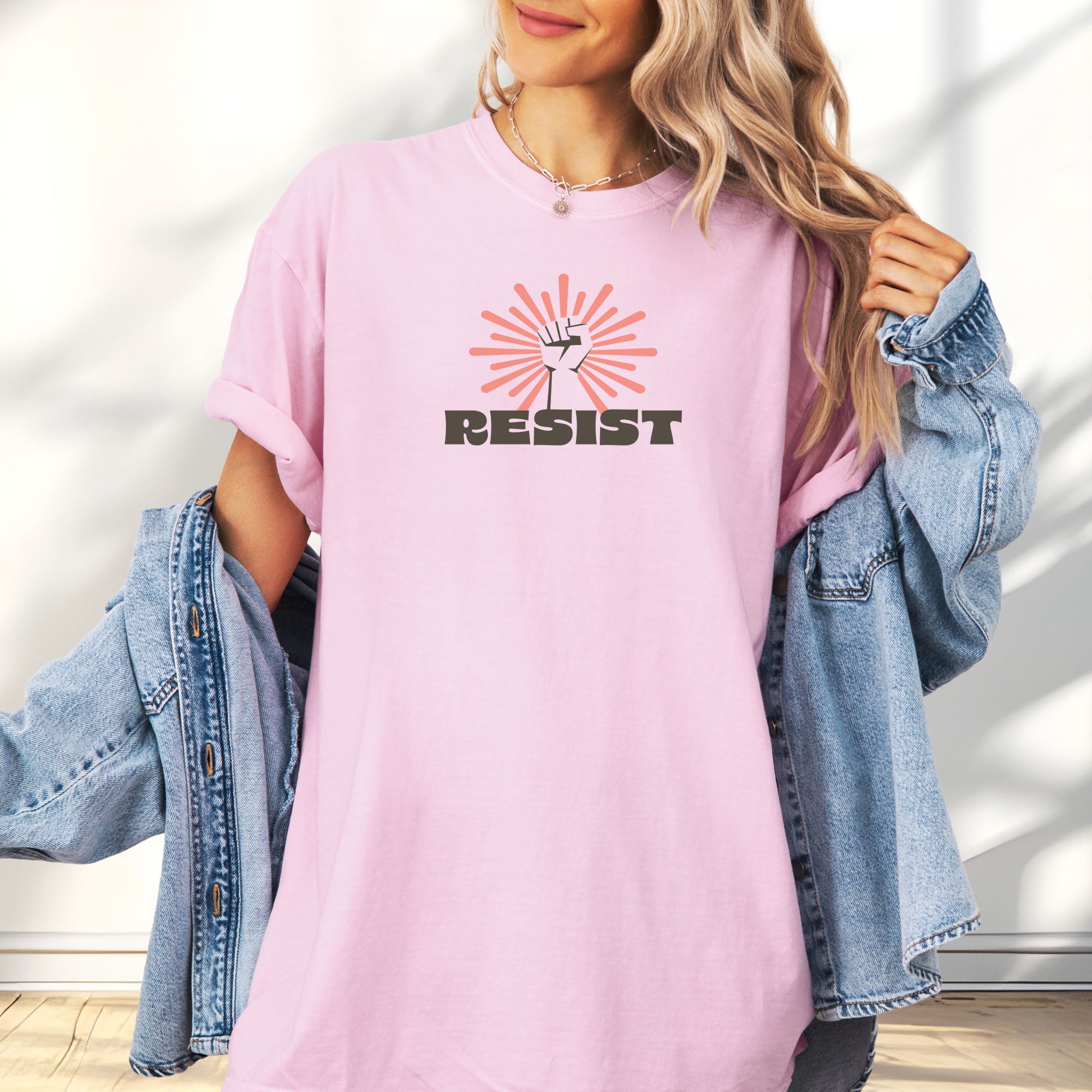 Female model wearing blossom t-shirt with retro style "resist" text, raised fist, and pinkish burst behind the fist.