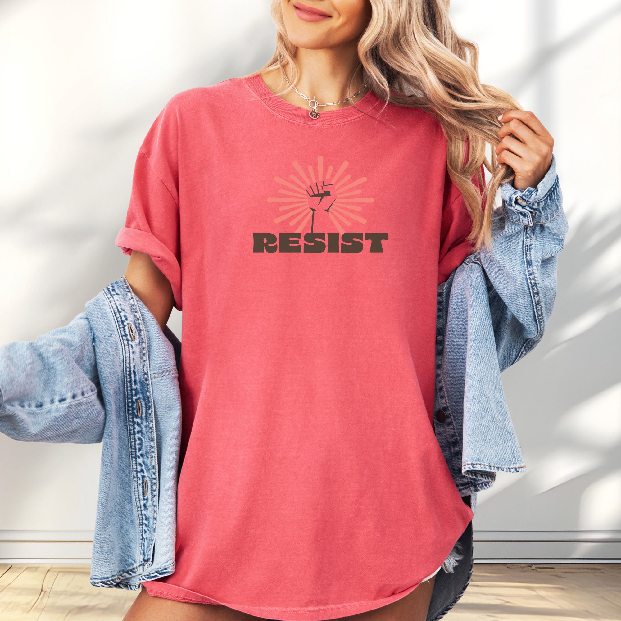 Female model wearing watermelon t-shirt with retro style "resist" text, raised fist, and pinkish burst behind the fist.