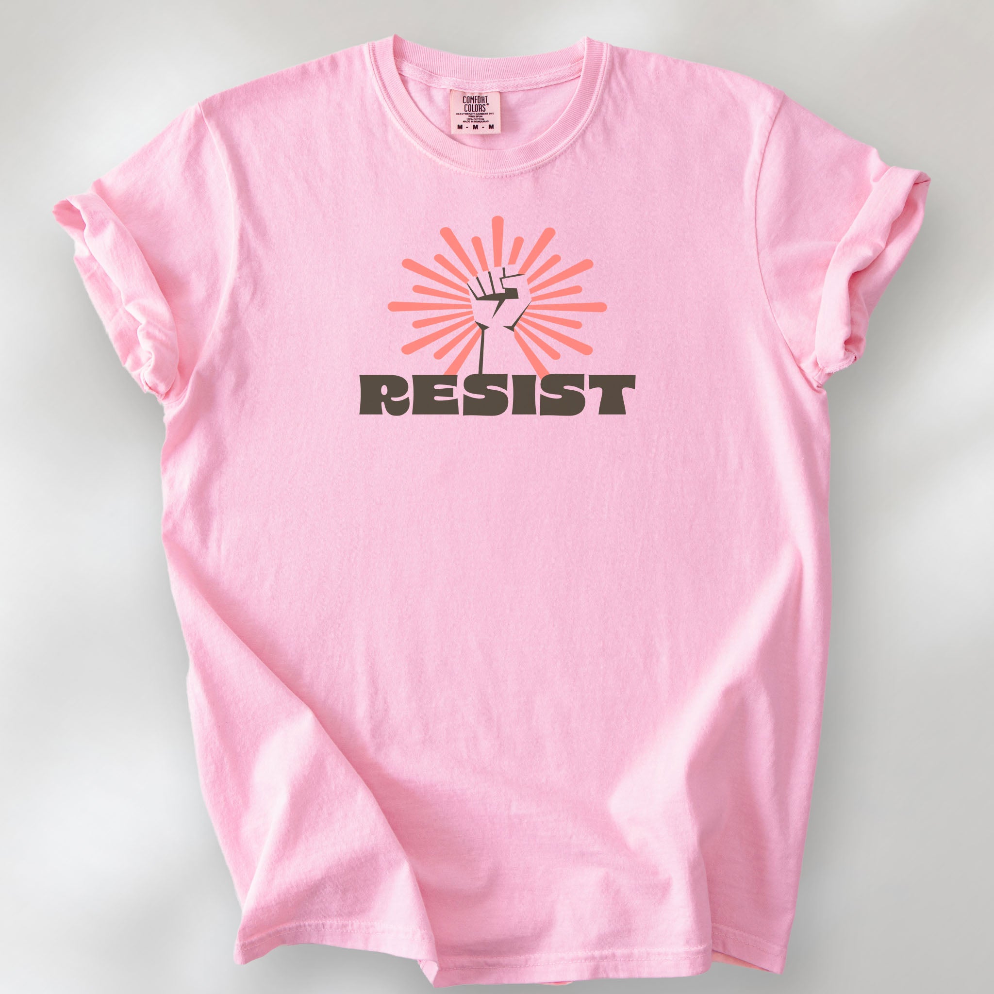Blossom t-shirt with retro style "resist" text, raised fist, and pinkish burst behind the fist.