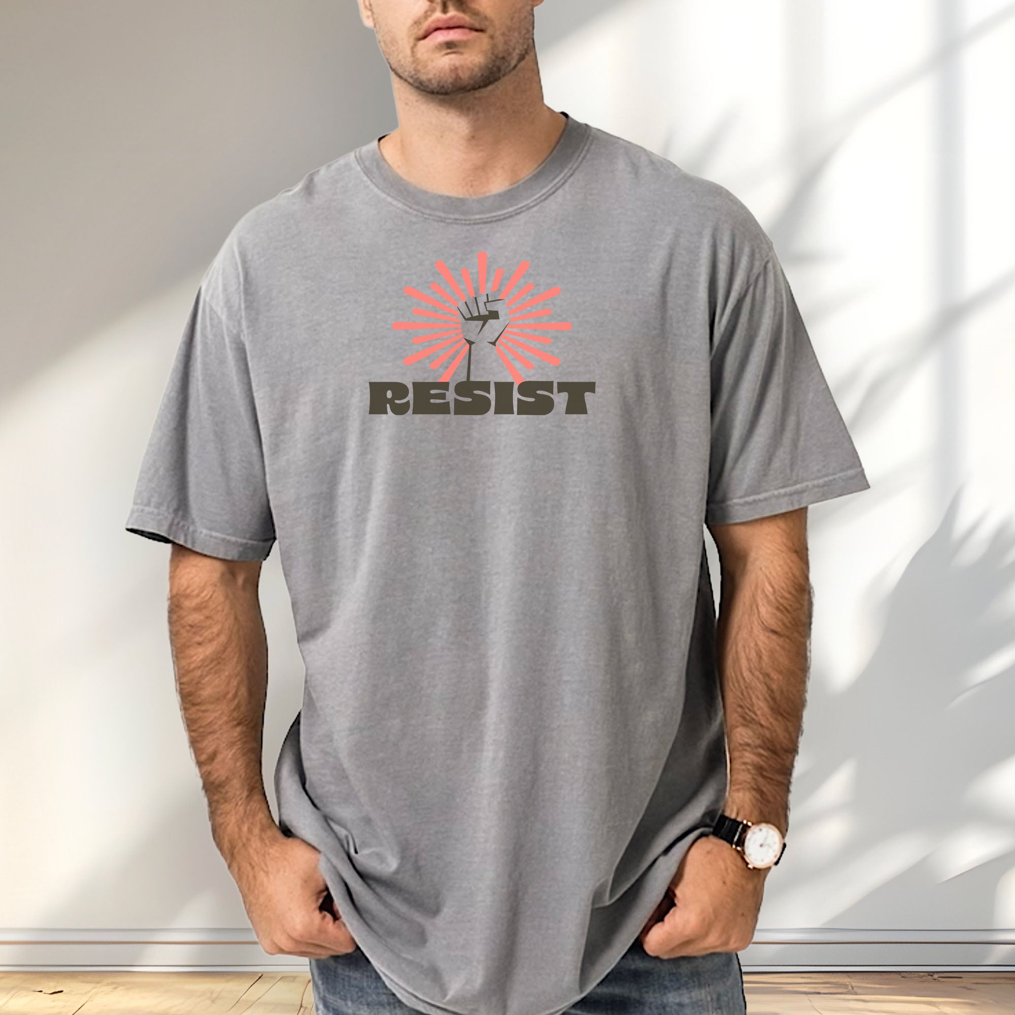 Male model wearing grey t-shirt with retro style "resist" text, raised fist, and pinkish burst behind the fist.