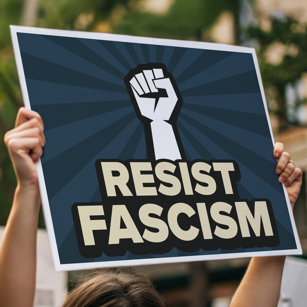 Protest sign with blue burst background and white raised fist above text that reads "Resist fascism" in all uppercase letters, held high in a crowd.