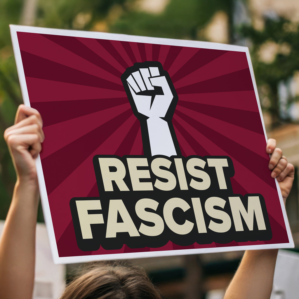 Protest sign with red burst background and white raised fist above text that reads "Resist fascism" in all uppercase letters, held high in a crowd.