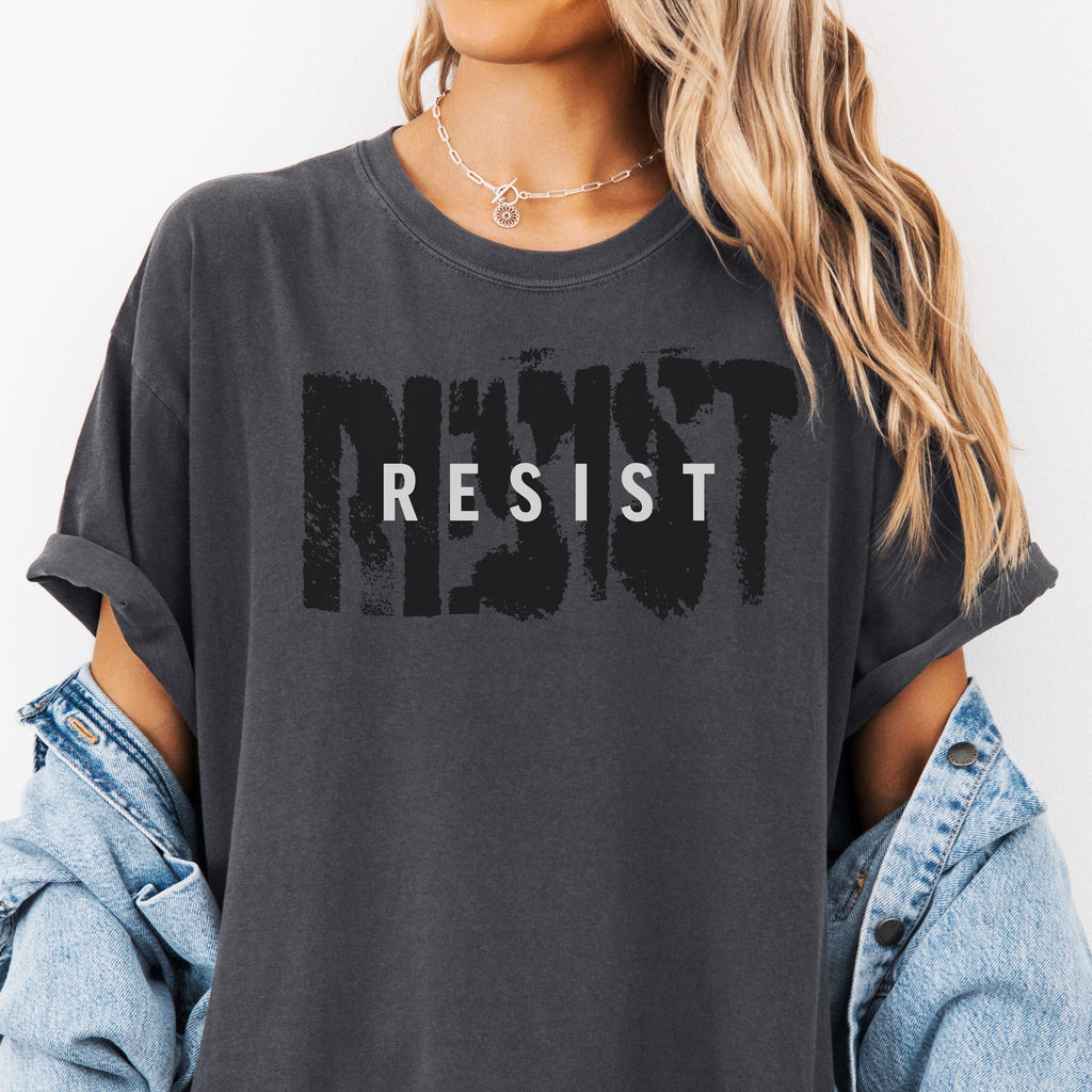 Female model wearing pepper t-shirt with the word "resist" atop the word "resist" in a grunge background texture.
