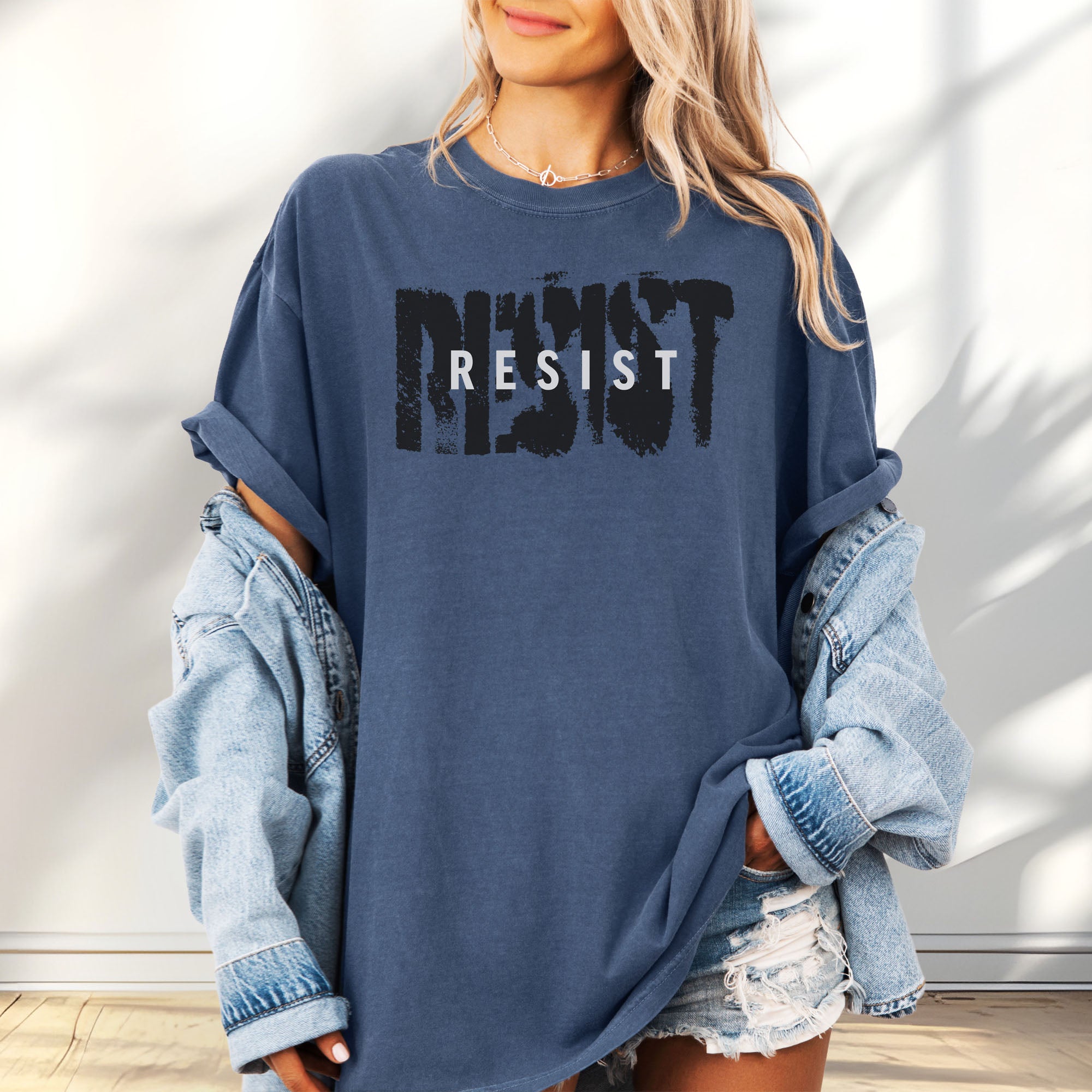 Female model wearing denim t-shirt with the word "resist" atop the word "resist" in a grunge background texture.