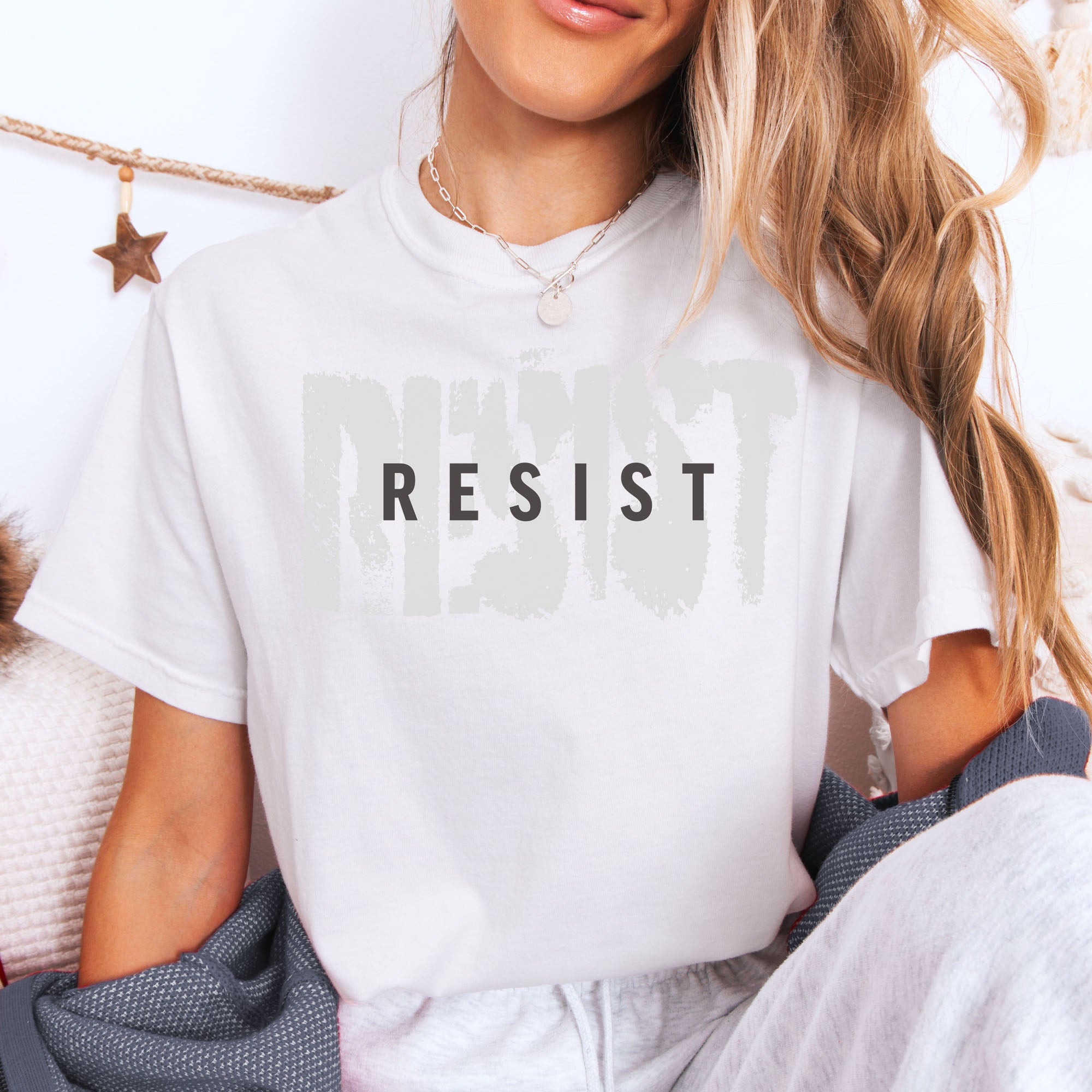 Female model wearing white t-shirt with the word "resist" atop the word "resist" in a grunge background texture.