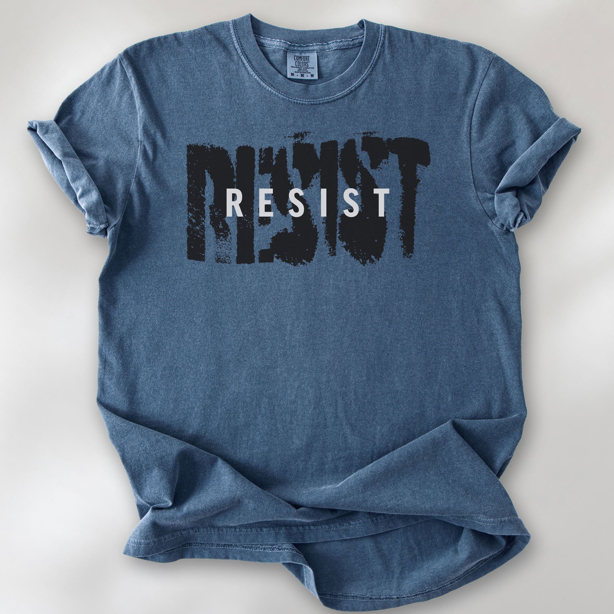 Denim t-shirt with the word "resist" atop the word "resist" in a grunge background texture.
