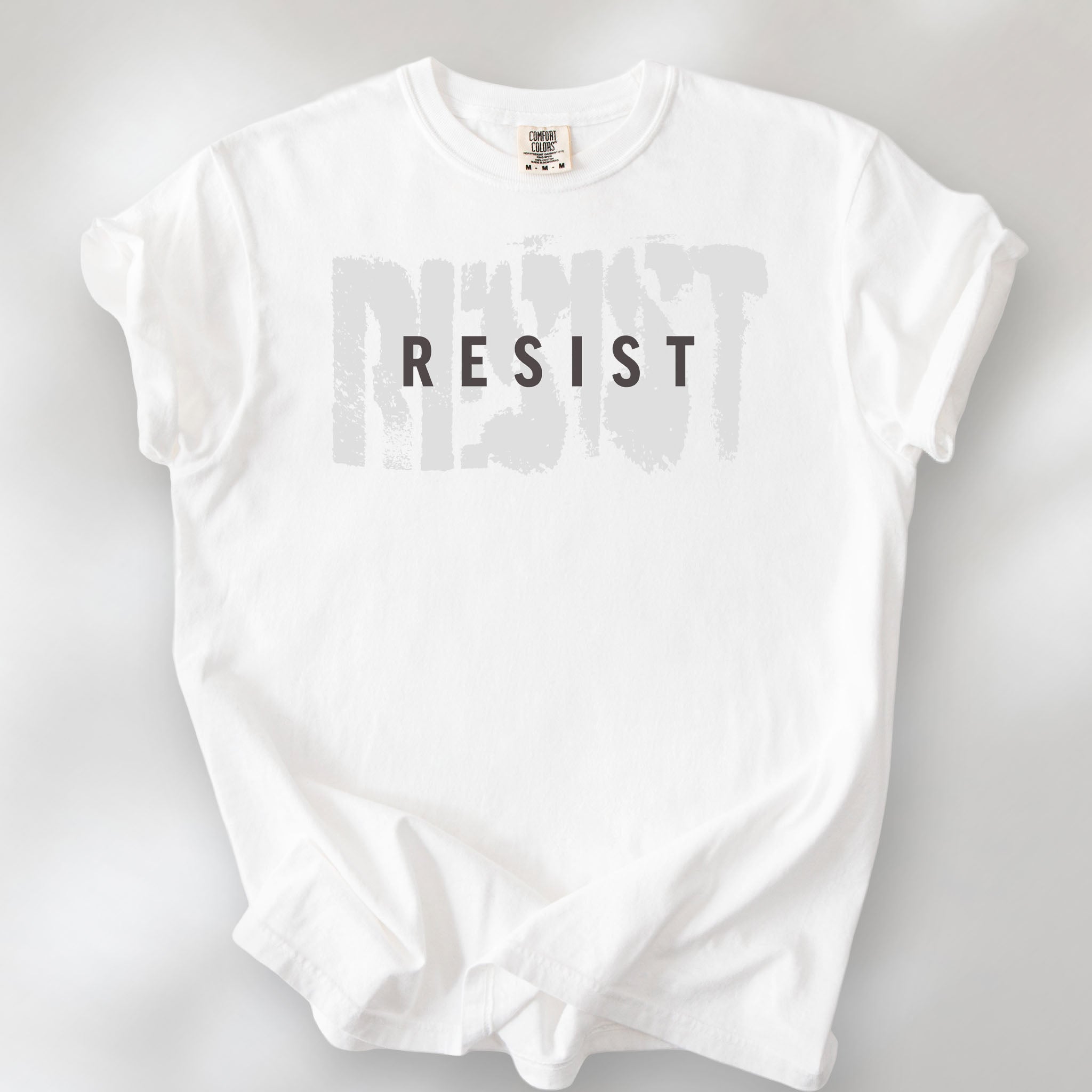 White t-shirt with the word "resist" atop the word "resist" in a grunge background texture.