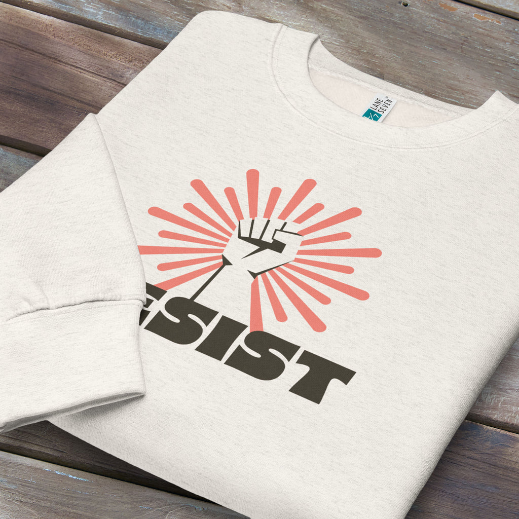 Folded oatmeal sweatshirt with retro style "resist" text, raised fist, and pinkish burst behind the fist.