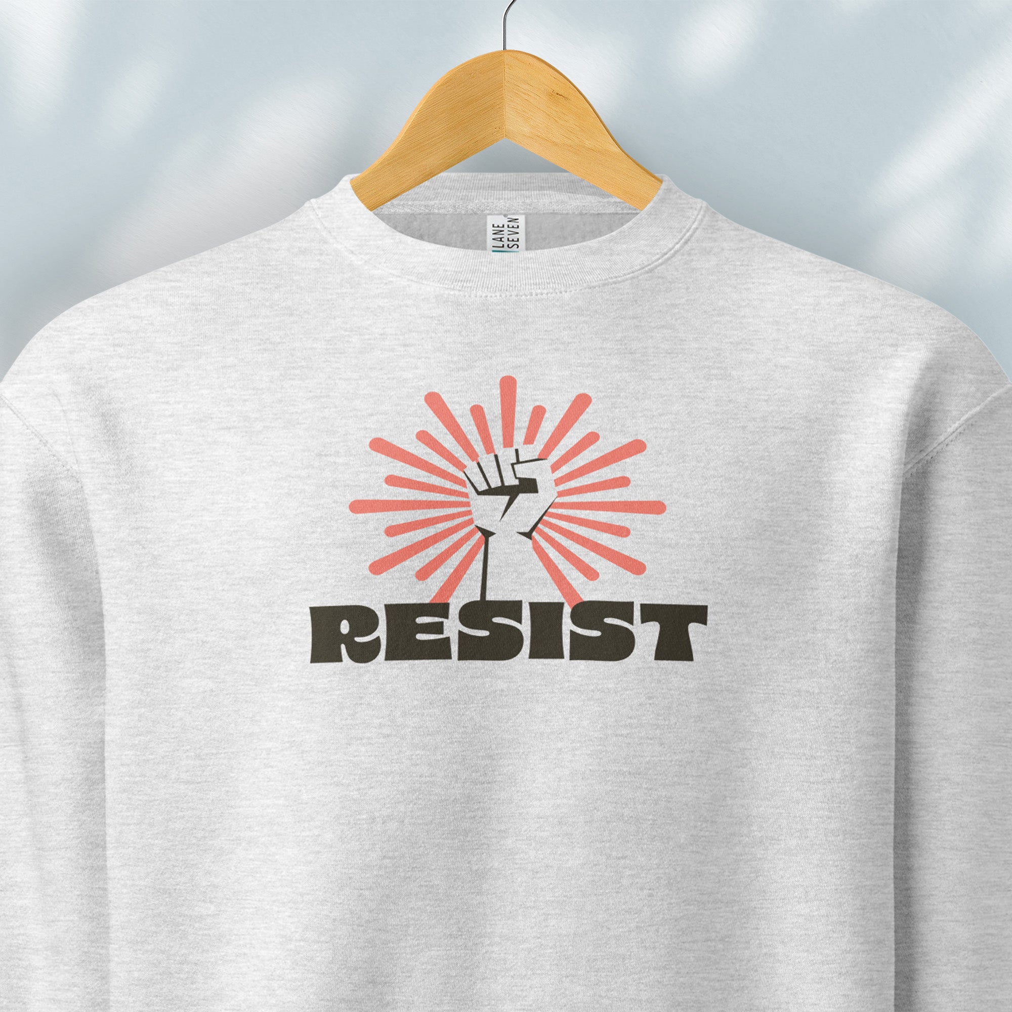 Hanging grey sweatshirt with retro style "resist" text, raised fist, and pinkish burst behind the fist.