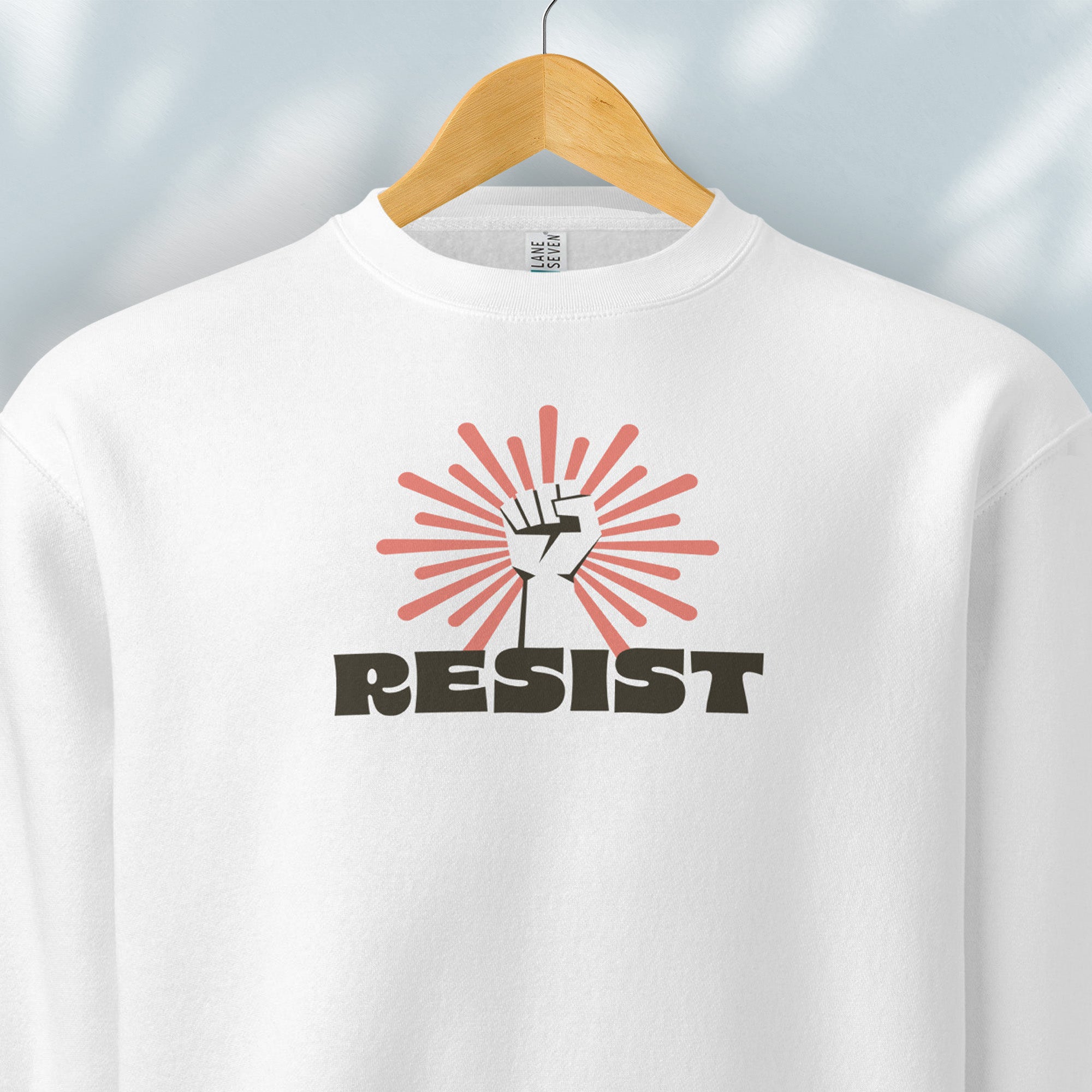 Hanging white sweatshirt with retro style "resist" text, raised fist, and pinkish burst behind the fist.