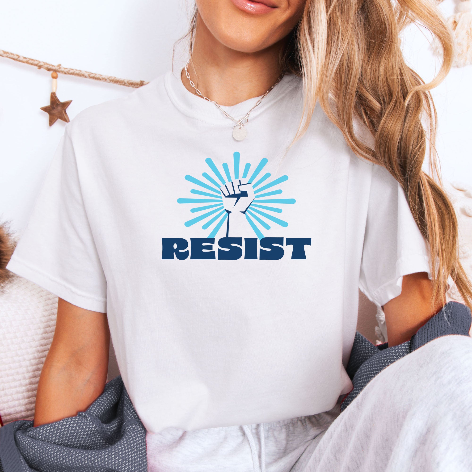 Female model wearing white t-shirt with blue Minnesota-themed “Resist” retro text and stylized raised fist design with burst.