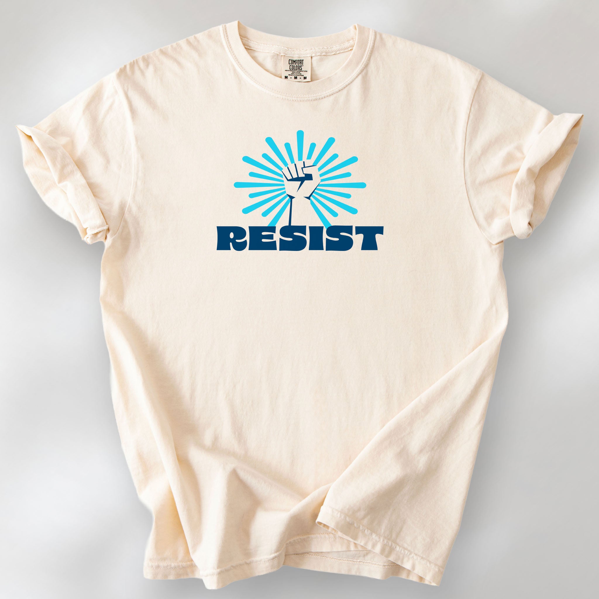 Ivory t-shirt with blue Minnesota-themed “Resist” retro text and stylized raised fist design with burst.