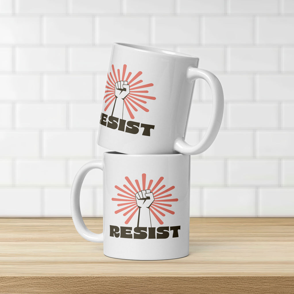 Two coffee mugs stacked, showing graphic on both sides of mug. Mug has a raised fist graphic in front of a coral burst, and bold retro-styled text that says "resist."