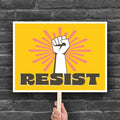 Printable protest sign with a white raised fist and the word “resist” in bold brown letters on a bright yellow background with pink radiating lines.
