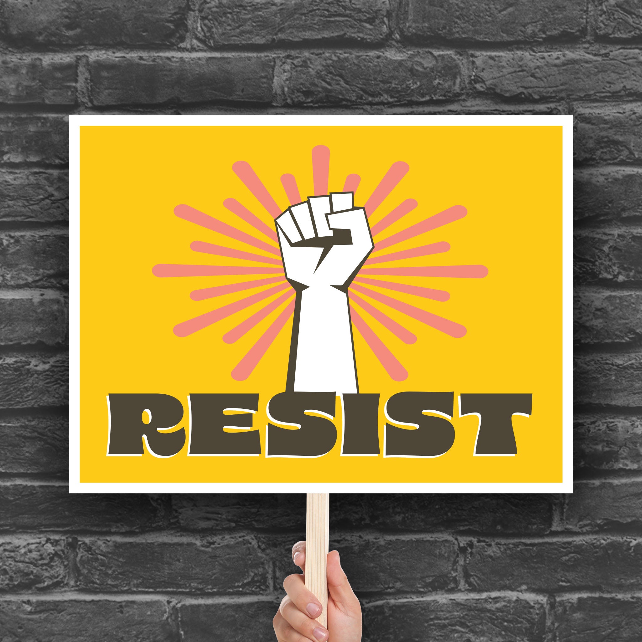 Printable protest sign with a white raised fist and the word “resist” in bold brown letters on a bright yellow background with pink radiating lines.