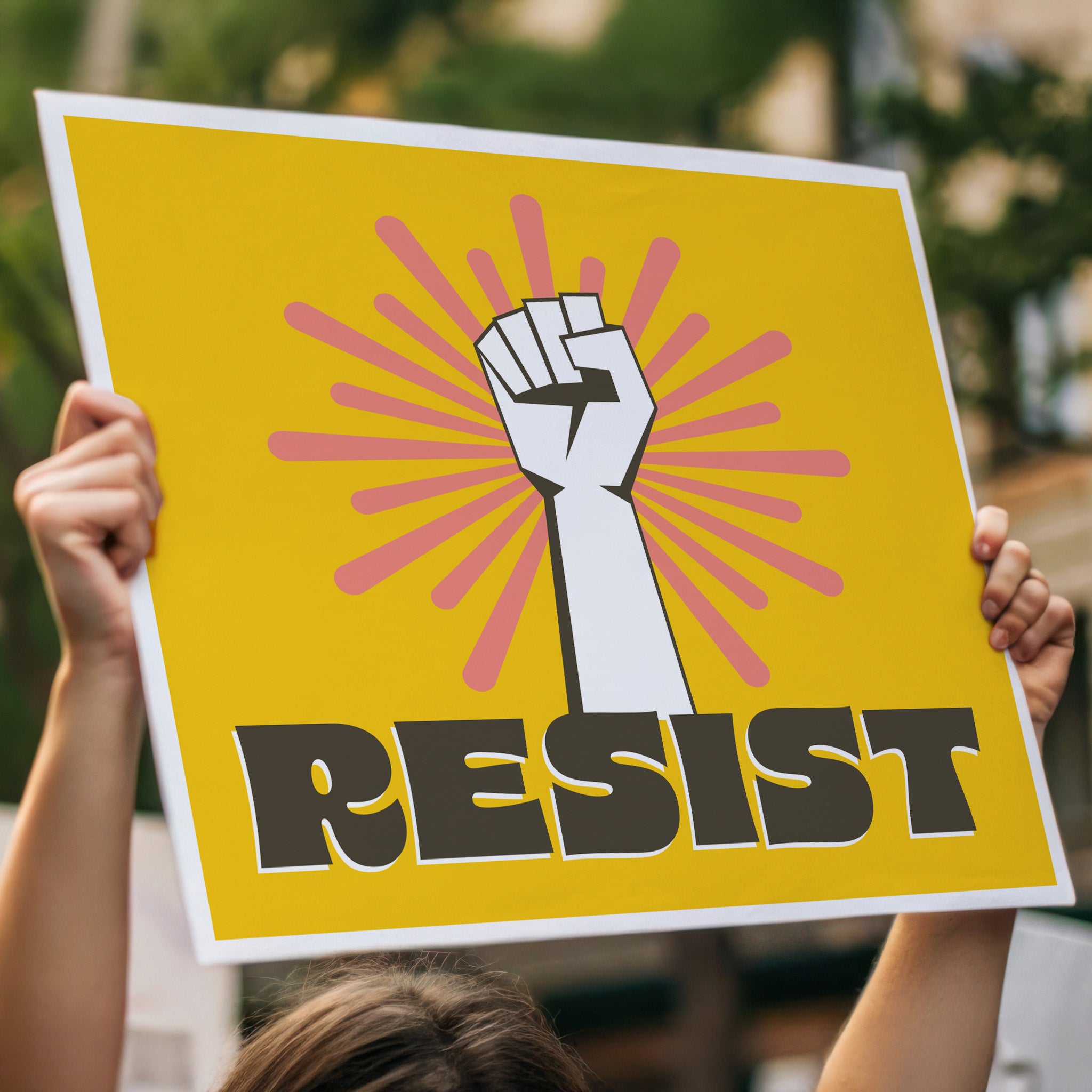 Printable protest sign with a white raised fist and the word “resist” in bold brown letters on a bright yellow background with pink radiating lines, held high above a person's head in a crowd.