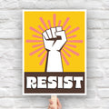 Downloadable, printable protest sign with yellow background behind a white raised fist and pink burst, with the retro-styled bold word "resist" below, reversed out of brown.