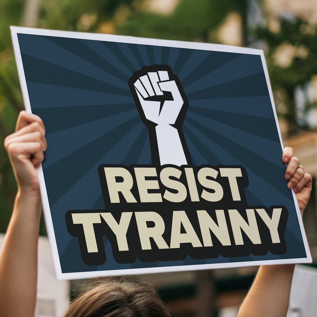 Aanti-Trump protest sign with bold gold text on a blue background hat reads "resist tyranny" below a raised fist, being held high in a crowd.