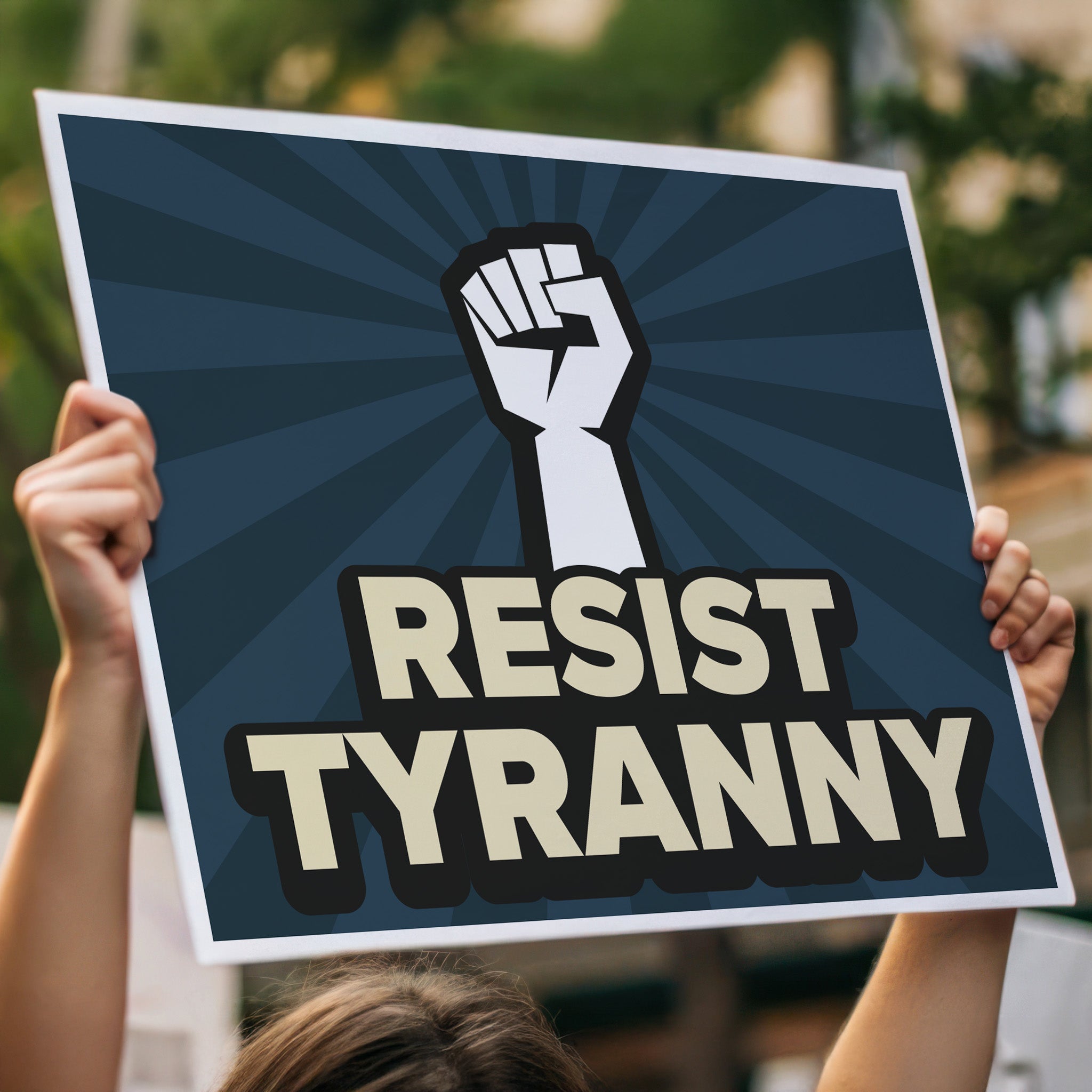 Aanti-Trump protest sign with bold gold text on a blue background hat reads "resist tyranny" below a raised fist, being held high in a crowd.