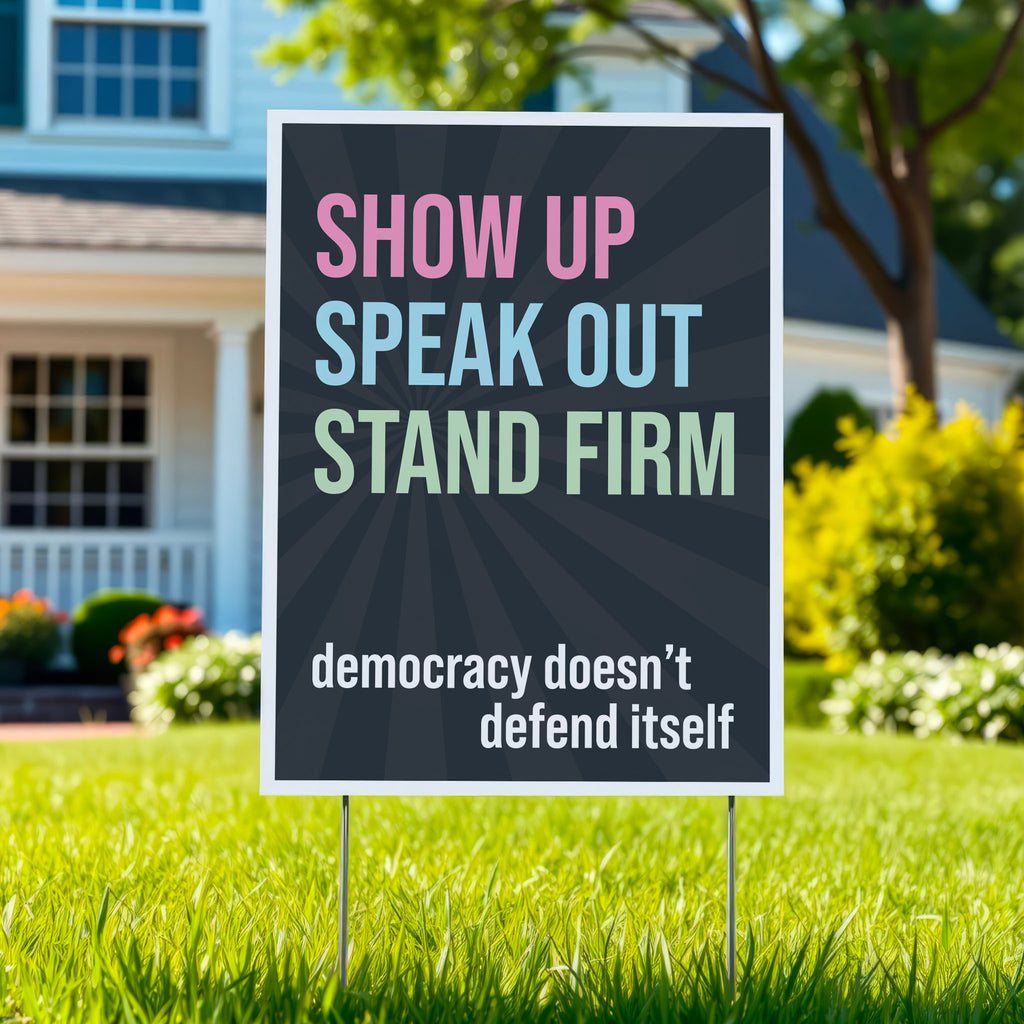 Yard sign with dark background with subtle burst, bold colorful text that reads "show up, speak out, stand firm", then white bold text that reads "democracy doesn't defend itself", planted in green lawn.