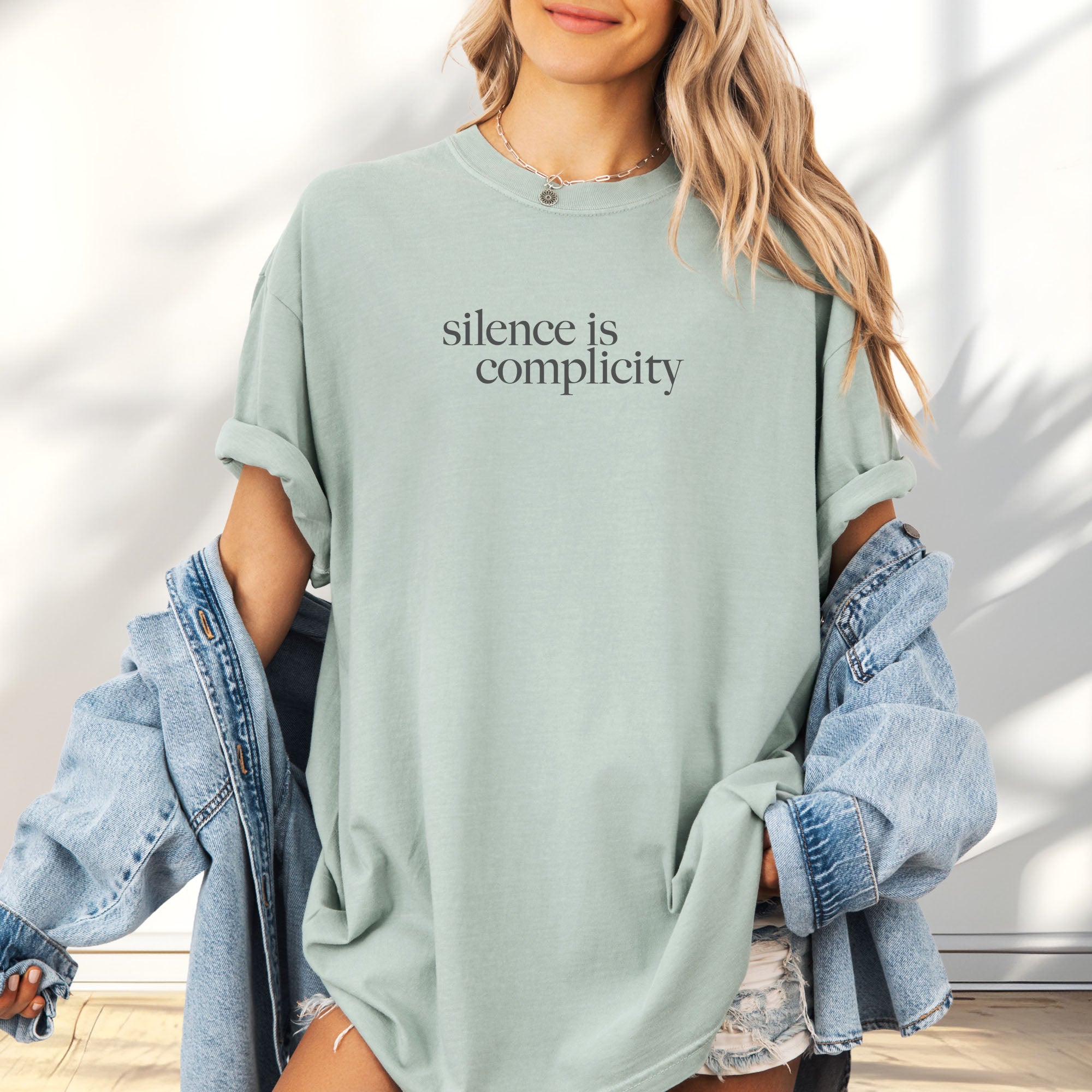 Female model wearing oversized bay t-shirt with minimalist serif text reading “silence is complicity."