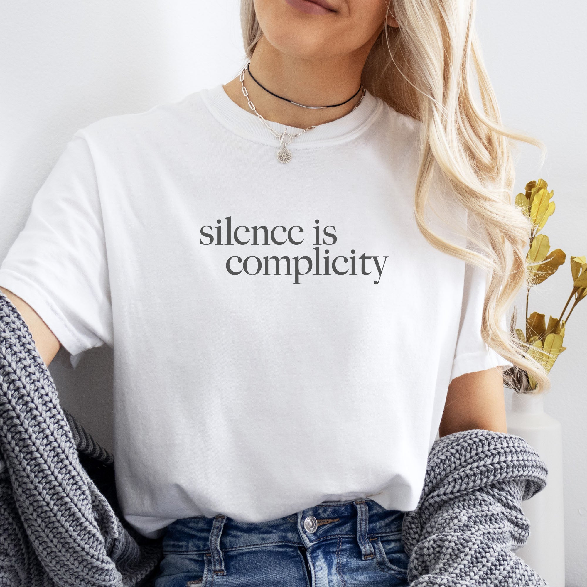 Female model wearing white t-shirt with minimalist serif text reading “silence is complicity.