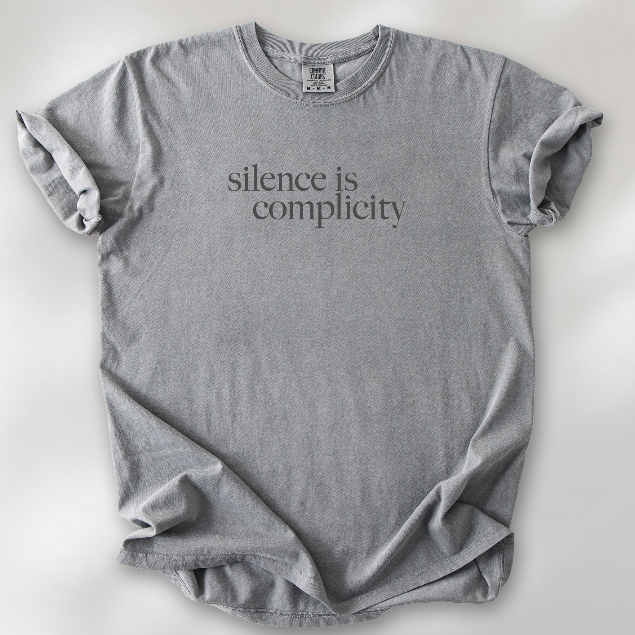 Grey t-shirt with minimalist serif text reading “silence is complicity."