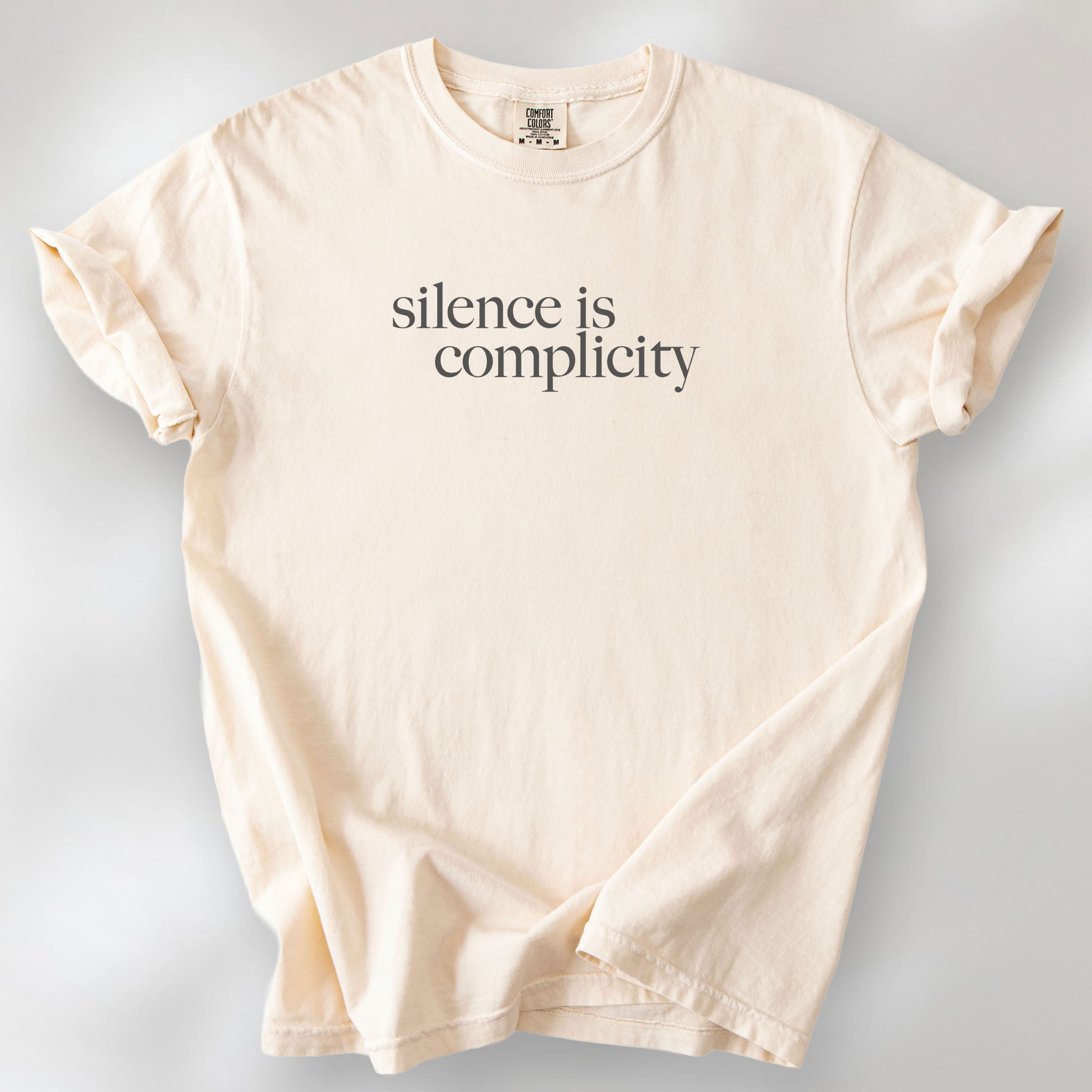 Ivory t-shirt with minimalist serif text reading “silence is complicity."