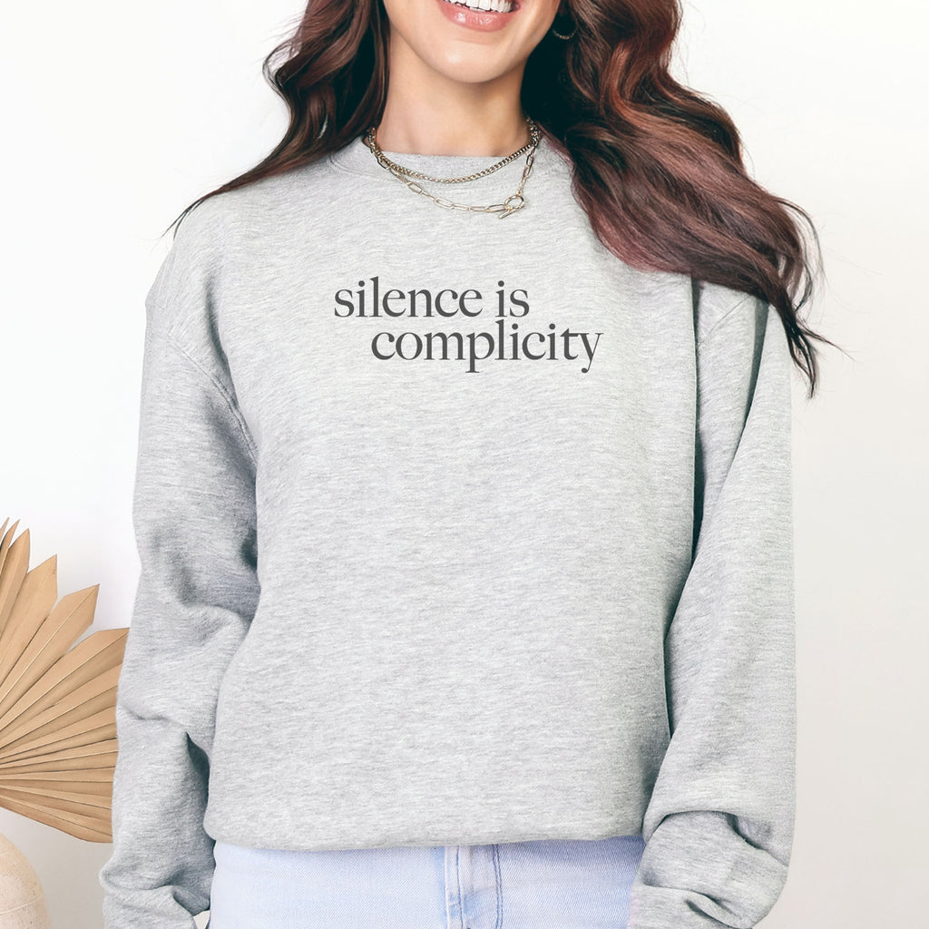 Female model wearing grey sweatshirt with minimalist serif text reading “silence is complicity."