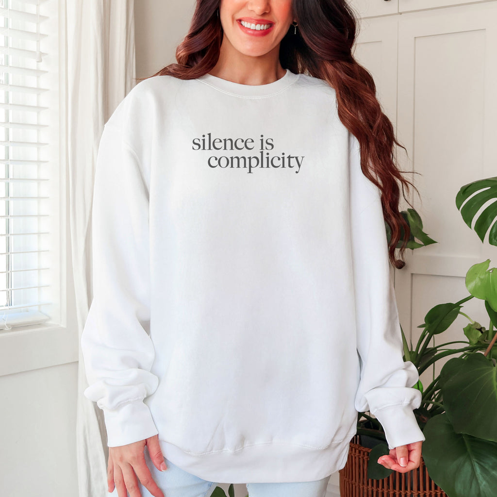 Female model wearing white sweatshirt with minimalist serif text reading “silence is complicity."