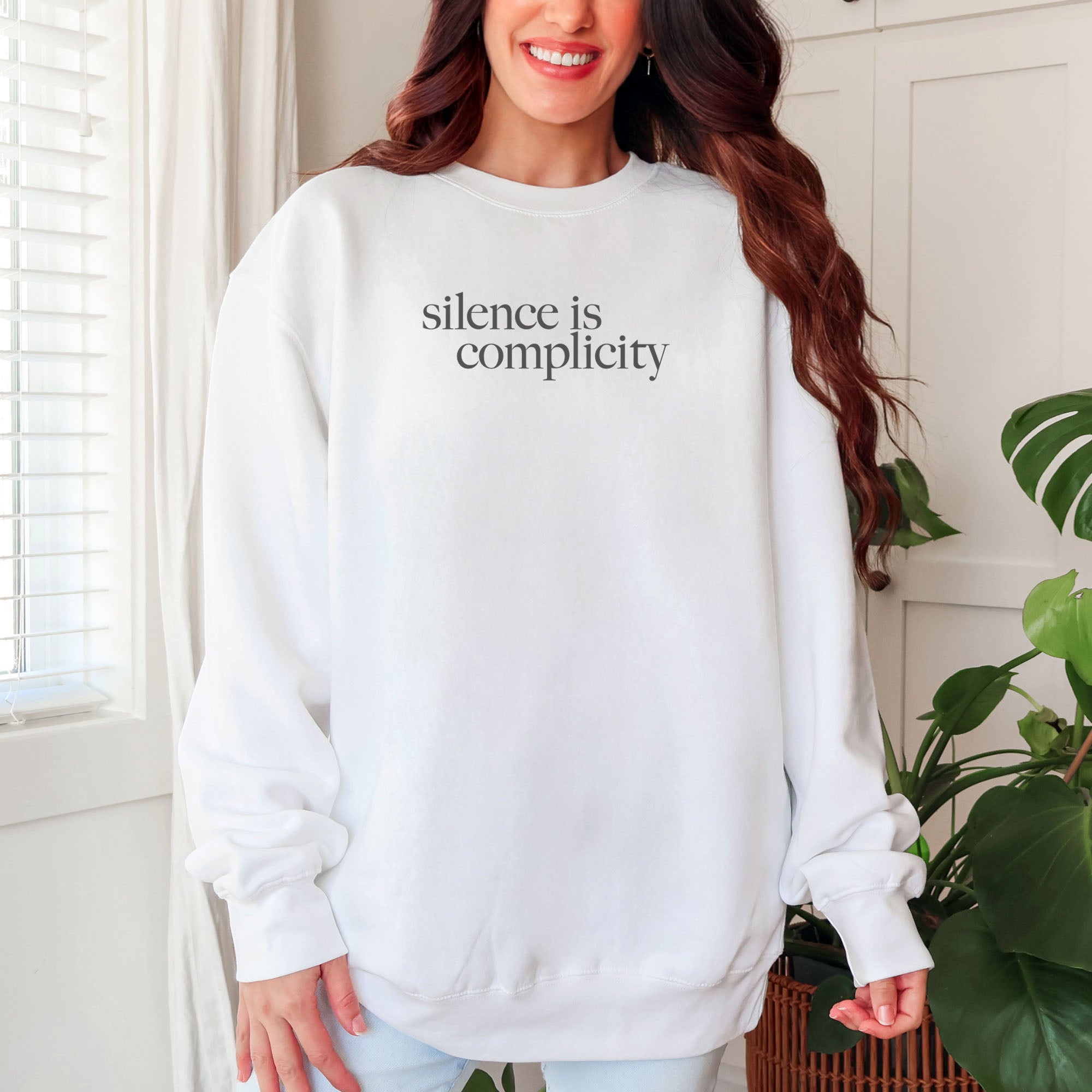 Female model wearing white sweatshirt with minimalist serif text reading “silence is complicity."