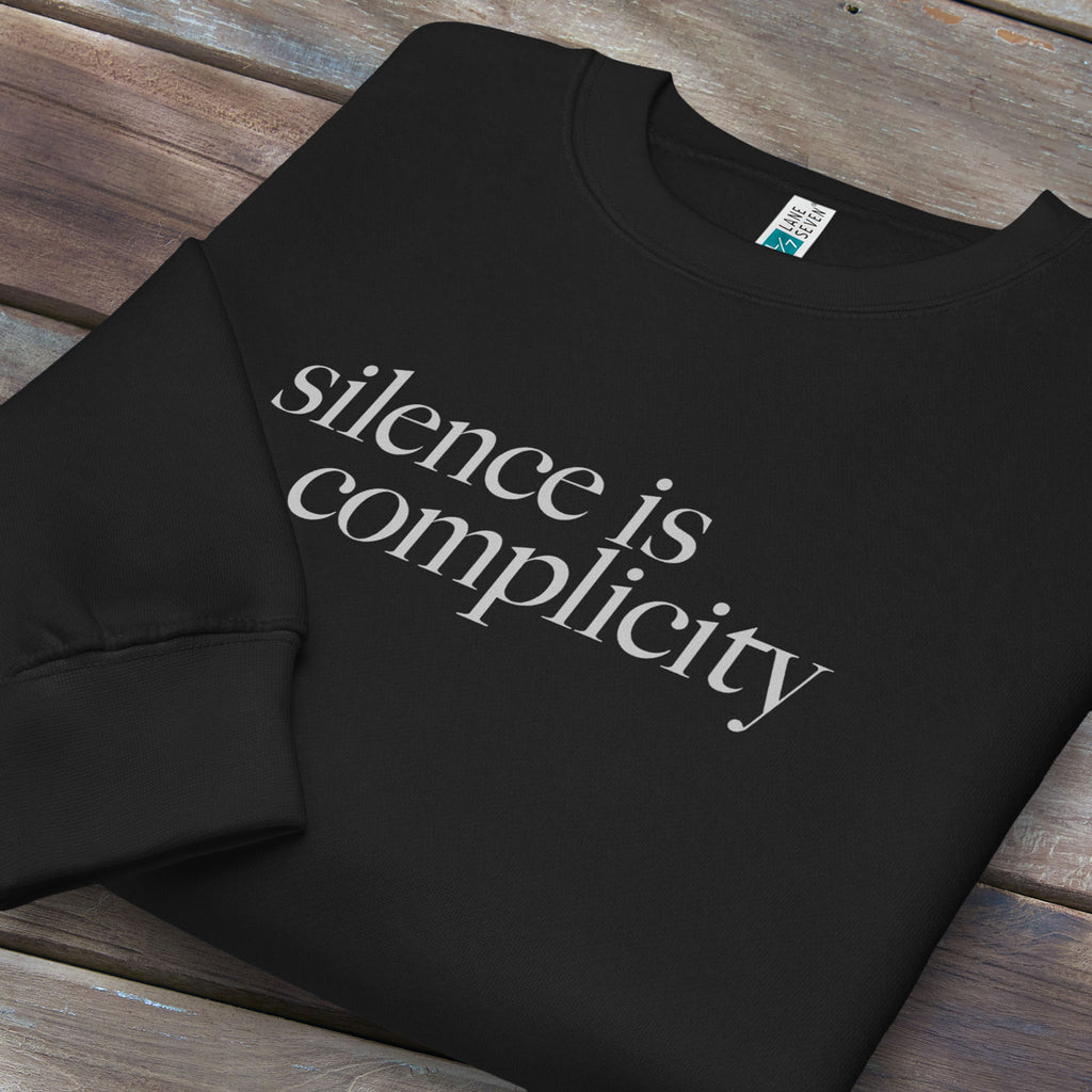 Folded black sweatshirt with minimalist serif text reading “silence is complicity."