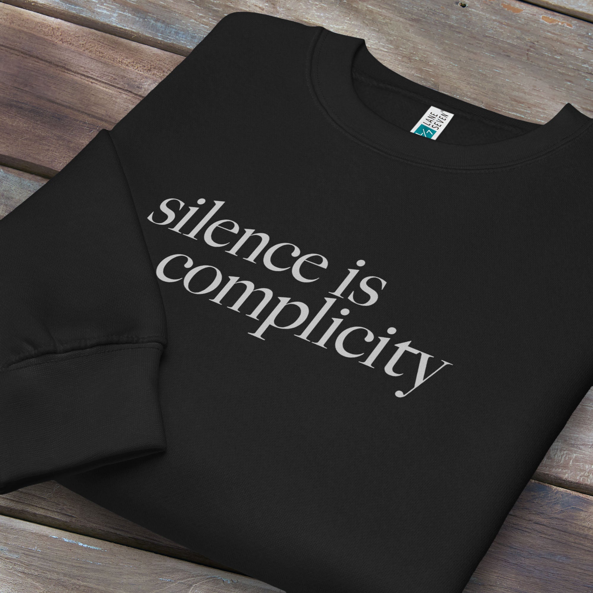Folded black sweatshirt with minimalist serif text reading “silence is complicity."