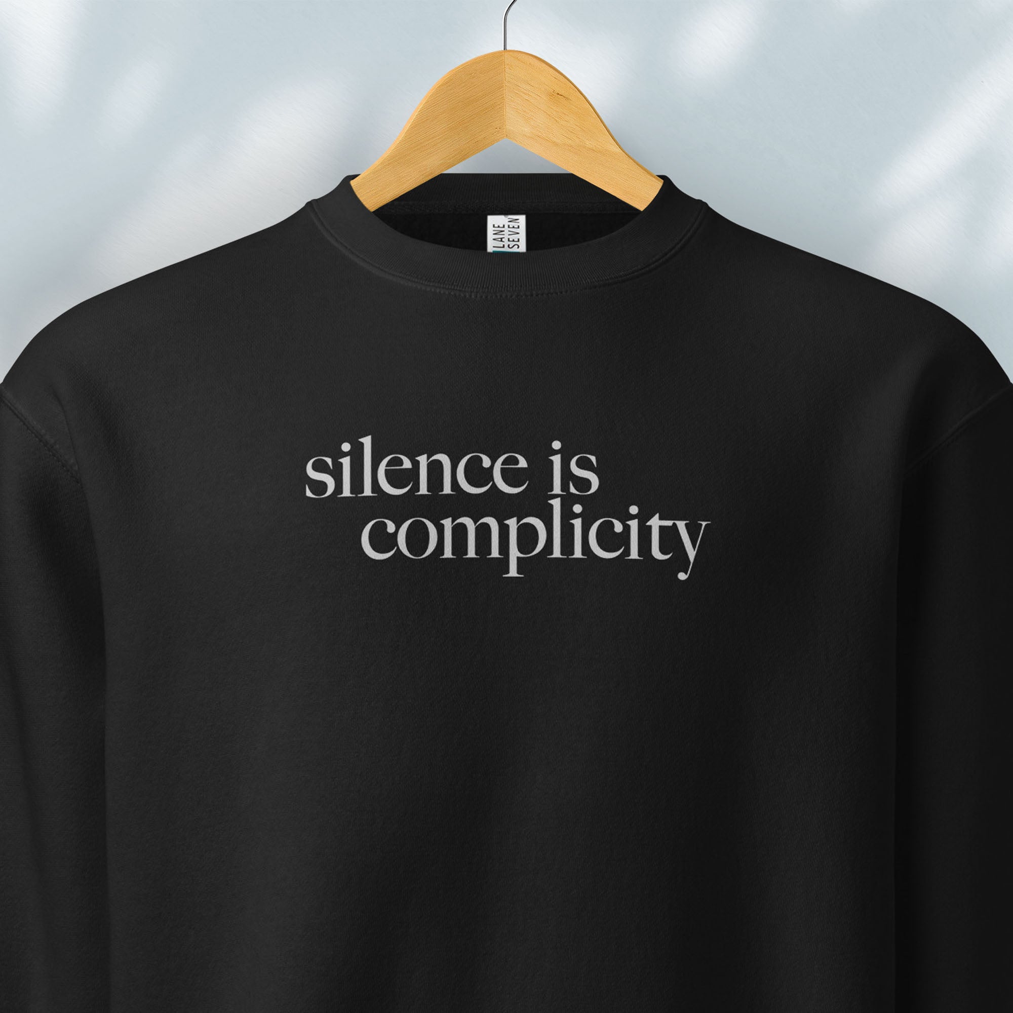 Hanging black sweatshirt with minimalist serif text reading “silence is complicity."