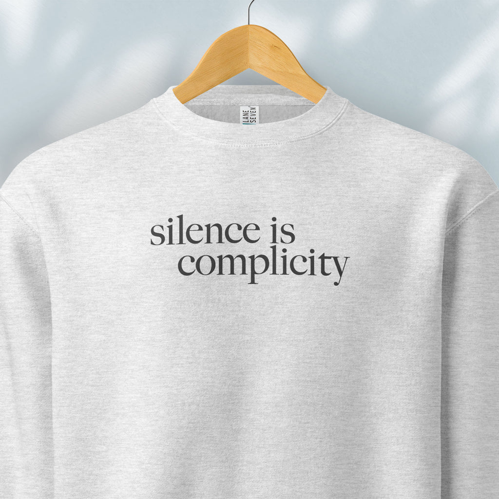 Hanging grey sweatshirt with minimalist serif text reading “silence is complicity."