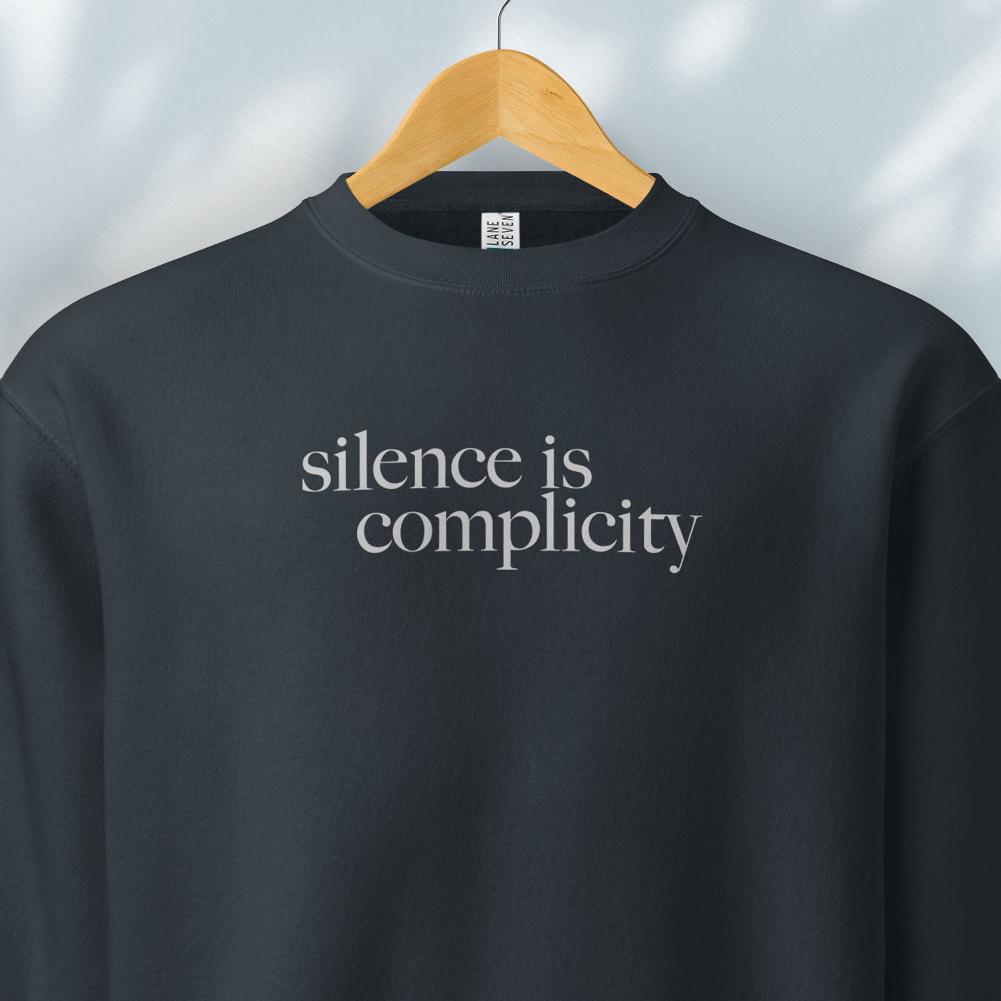 Hanging navy sweatshirt with minimalist serif text reading “silence is complicity."
