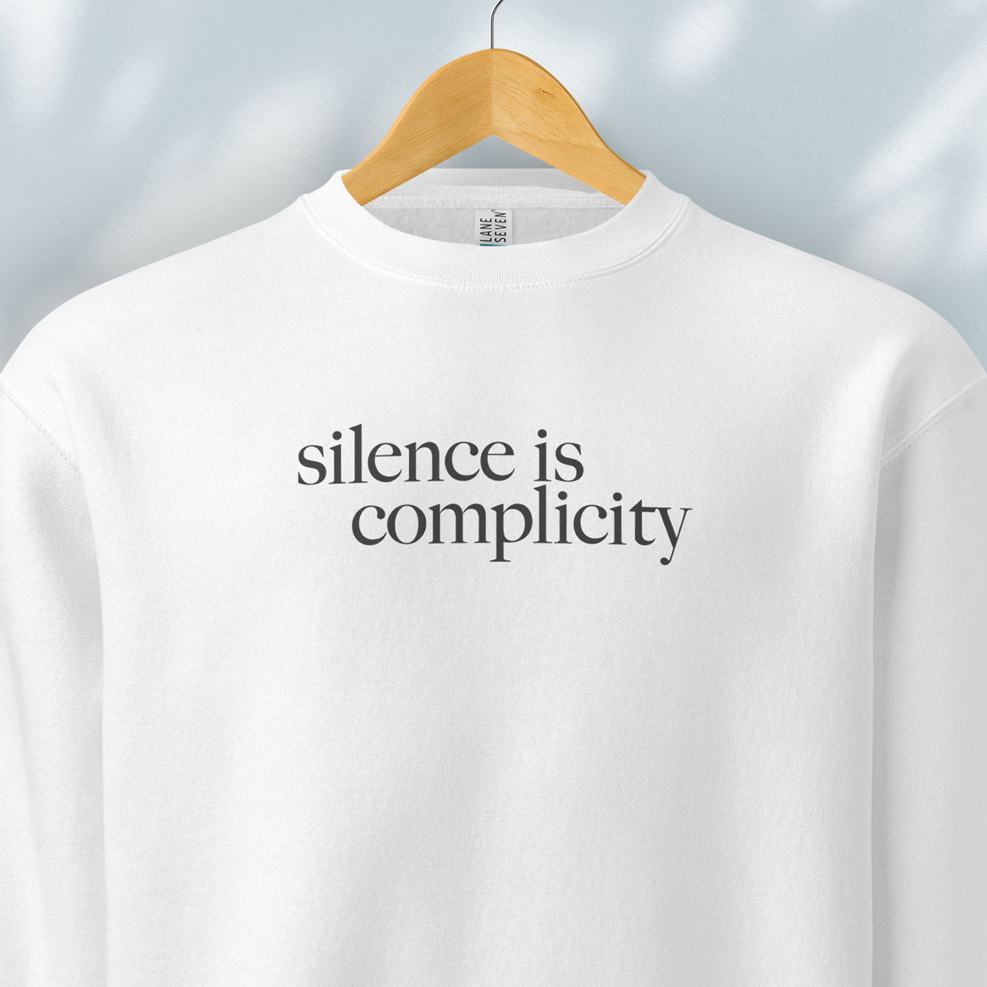 Hanging white sweatshirt with minimalist serif text reading “silence is complicity."