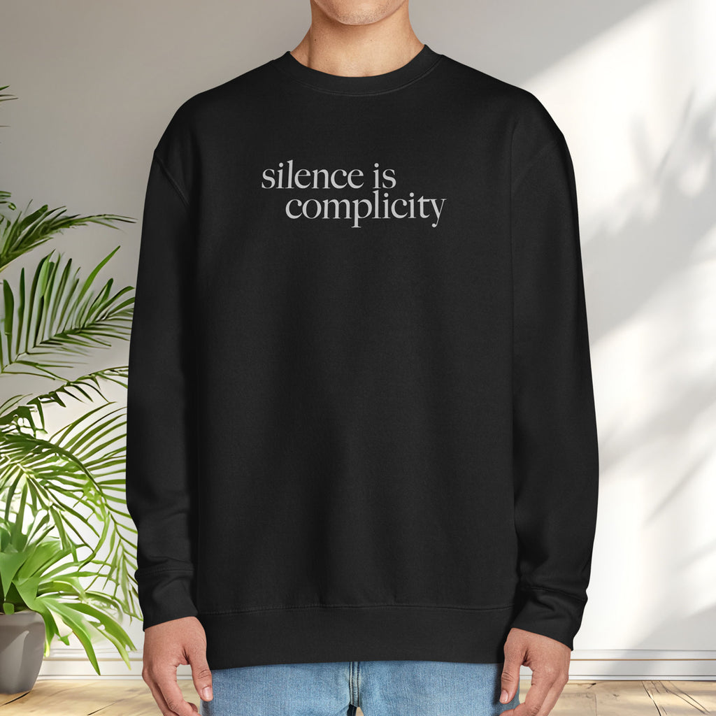 Male model wearing black sweatshirt with minimalist serif text reading “silence is complicity."
