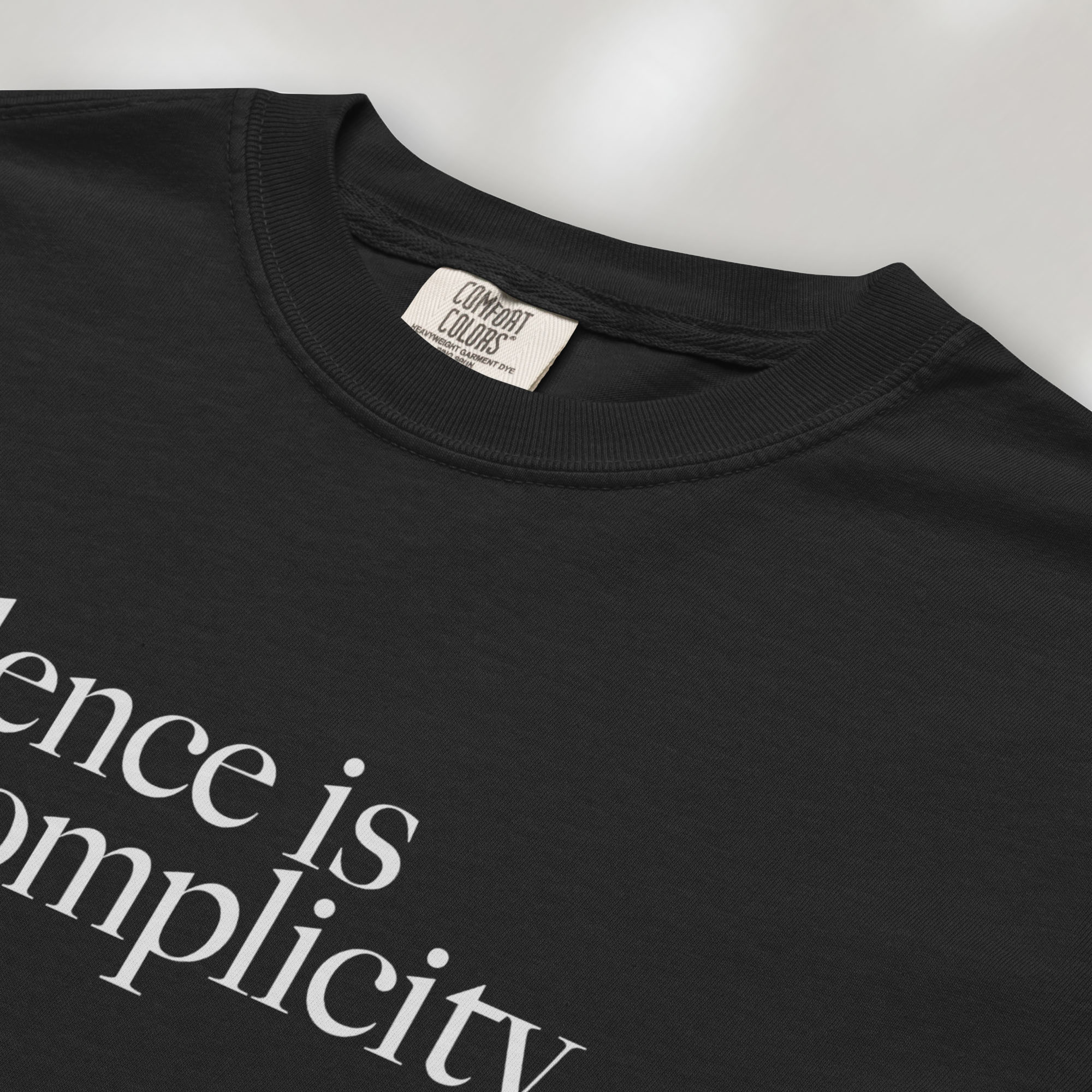 Closeup detail of black t-shirt with minimalist serif text reading “silence is complicity."
