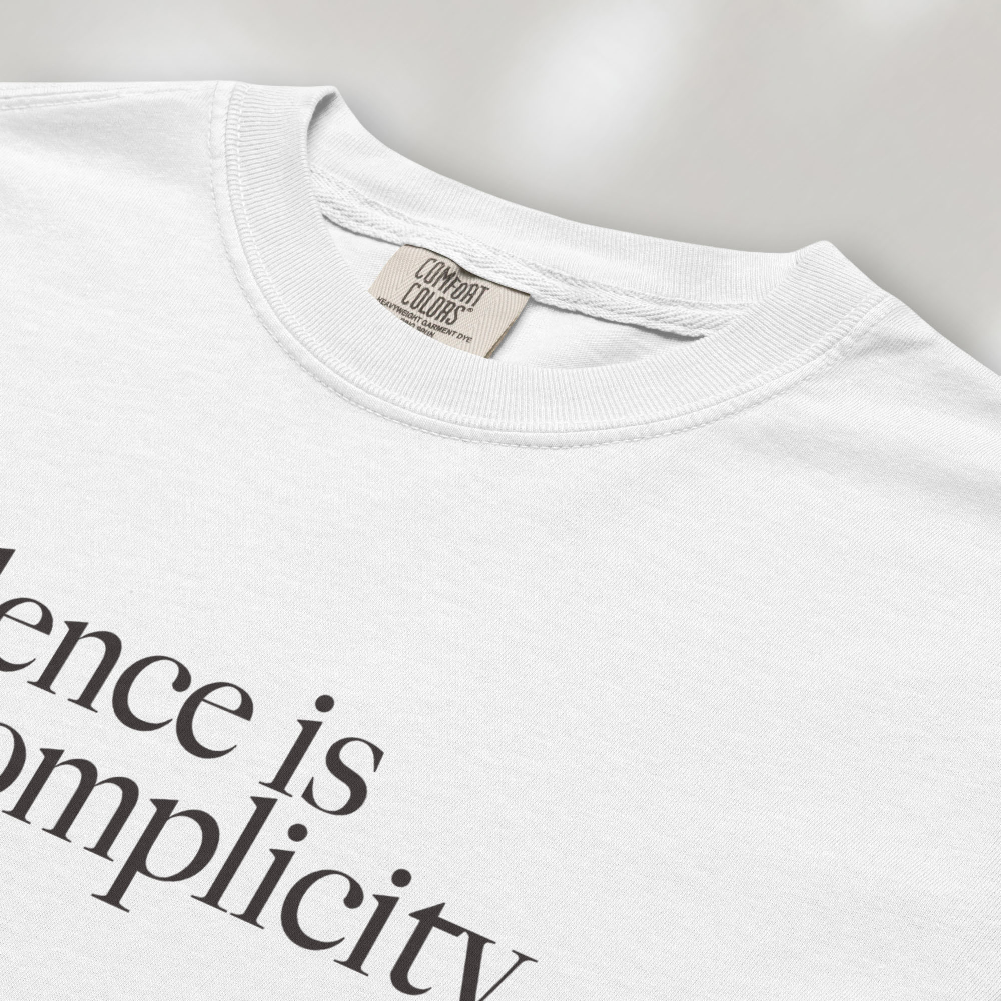 Closeup detail of white t-shirt with minimalist serif text reading “silence is complicity."
