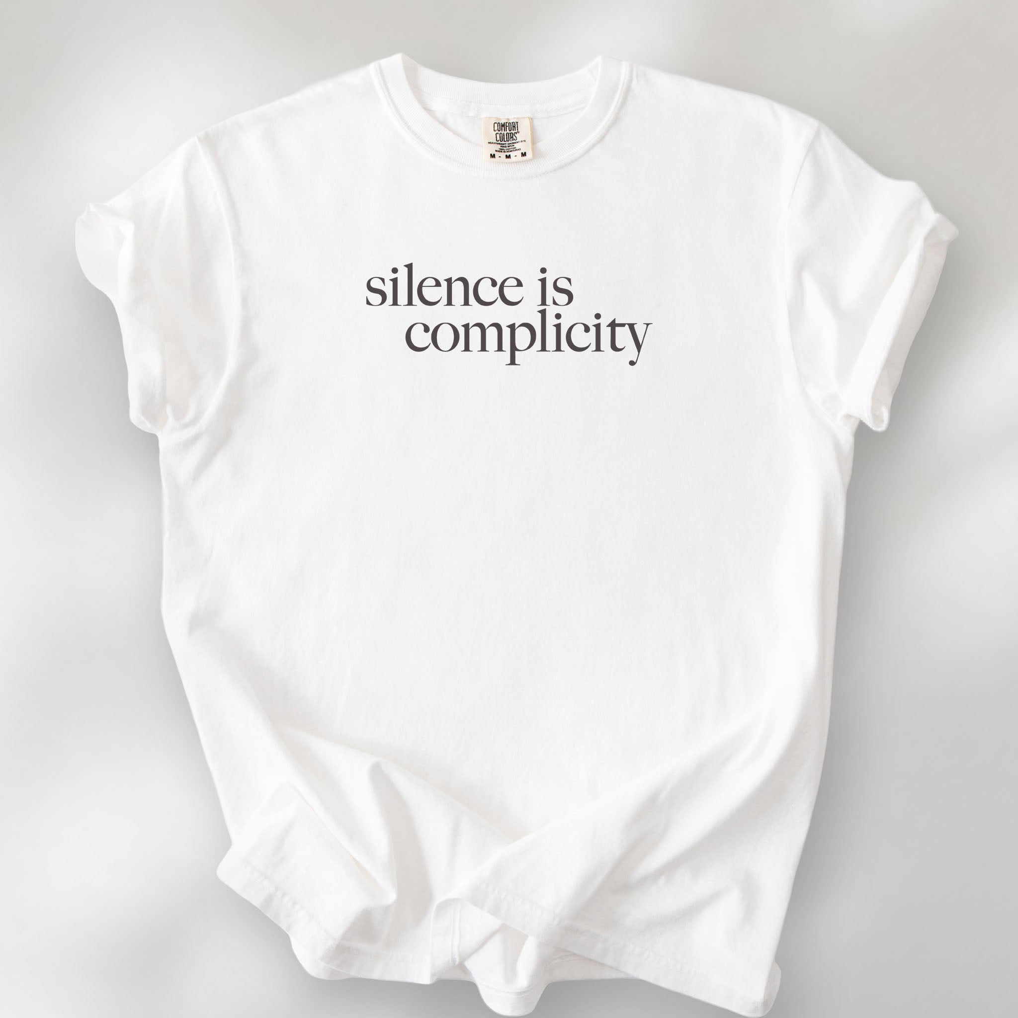 White t-shirt with minimalist serif text reading “silence is complicity."