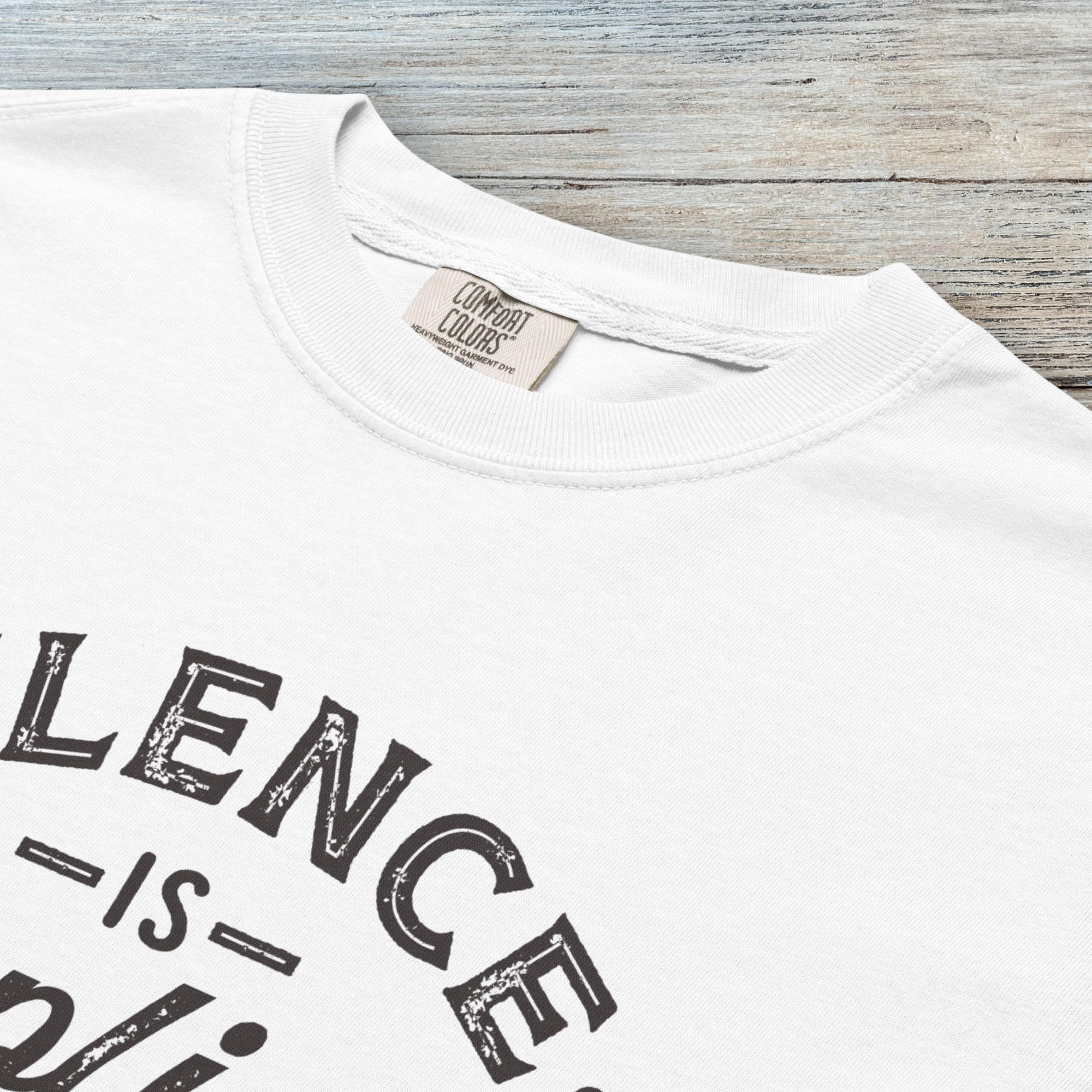 Closeup detail of white t-shirt with vintage distressed typography reading “Silence Is Complicity – Show Up Speak Out.”