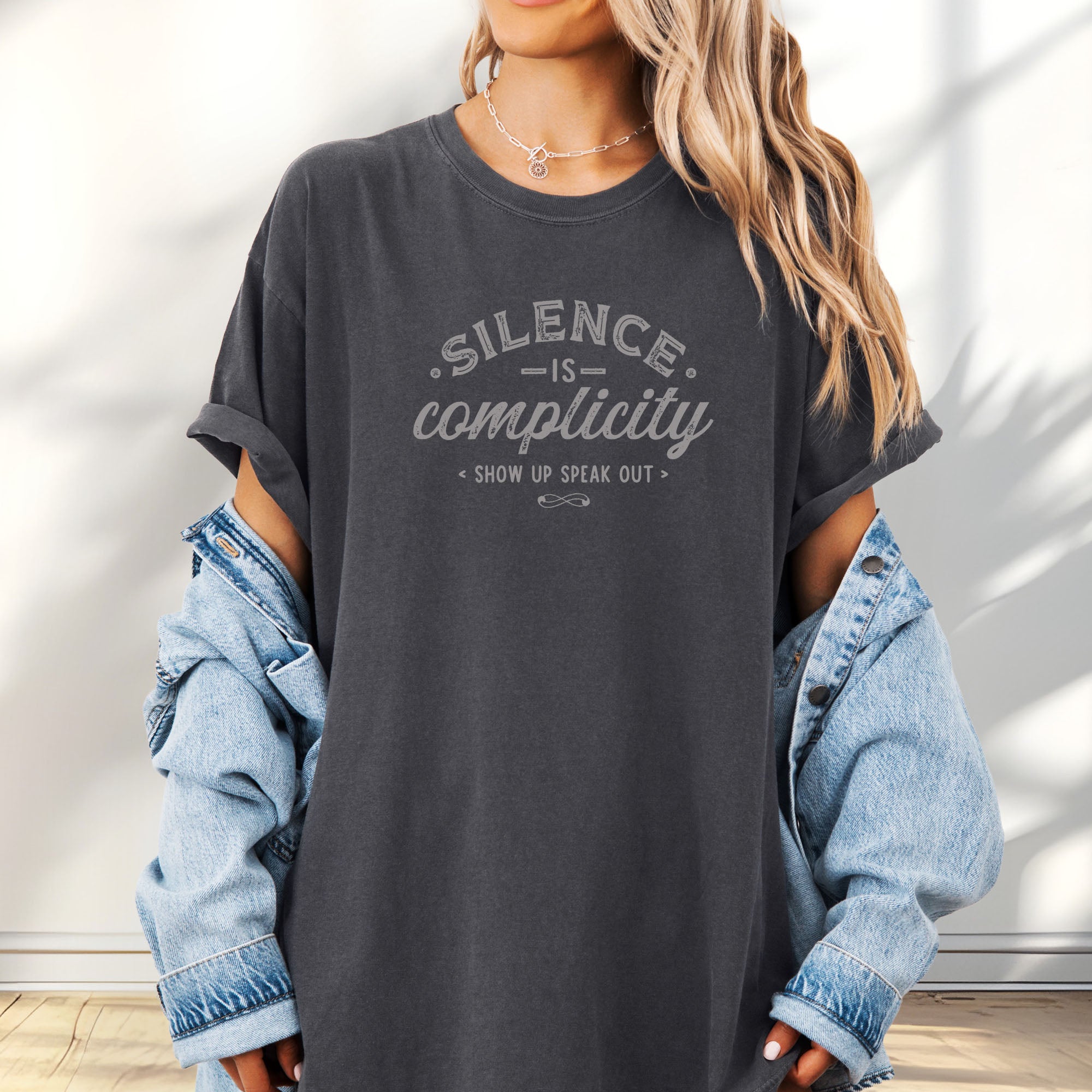 Female model wearing oversized pepper t-shirt with vintage distressed typography reading “Silence Is Complicity – Show Up Speak Out.”