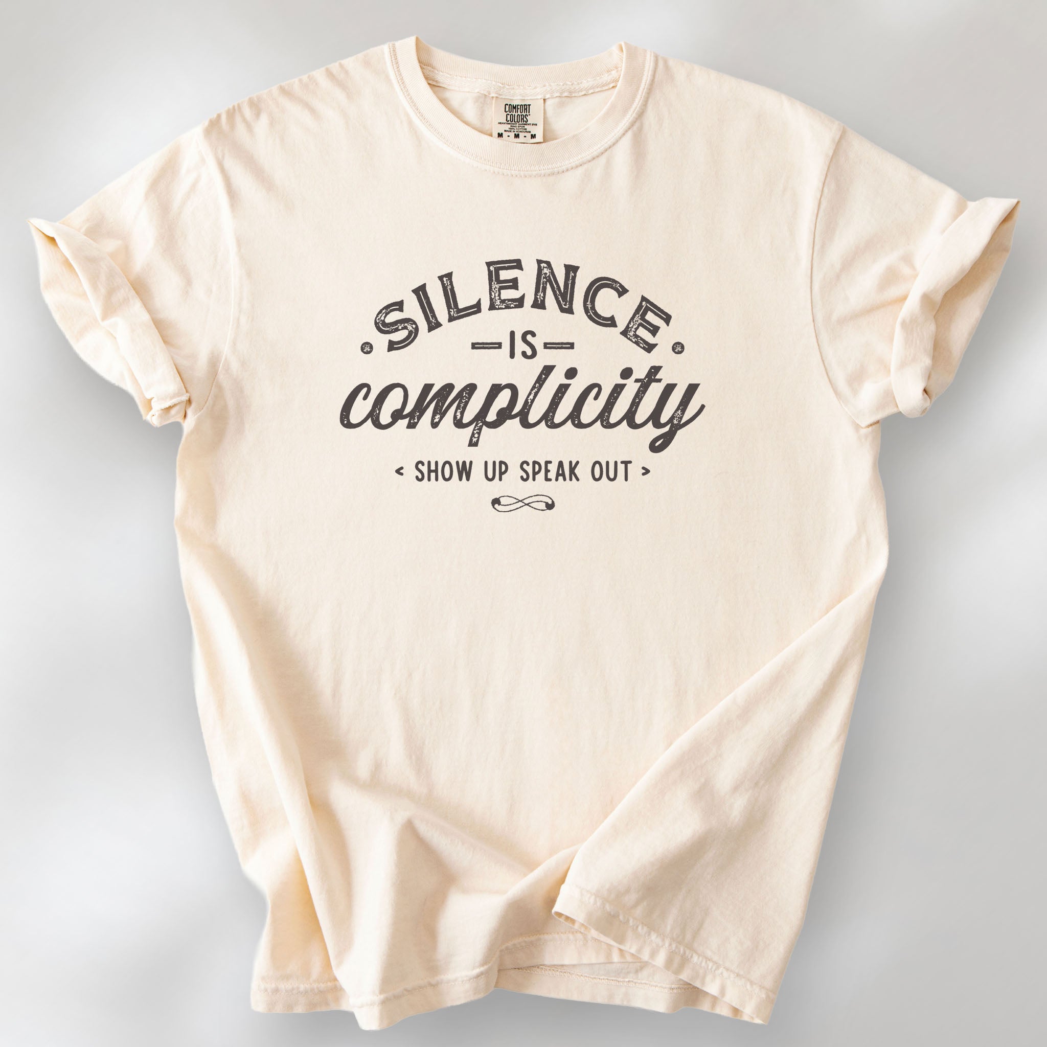 Ivory t-shirt with vintage distressed typography reading “Silence Is Complicity – Show Up Speak Out.”