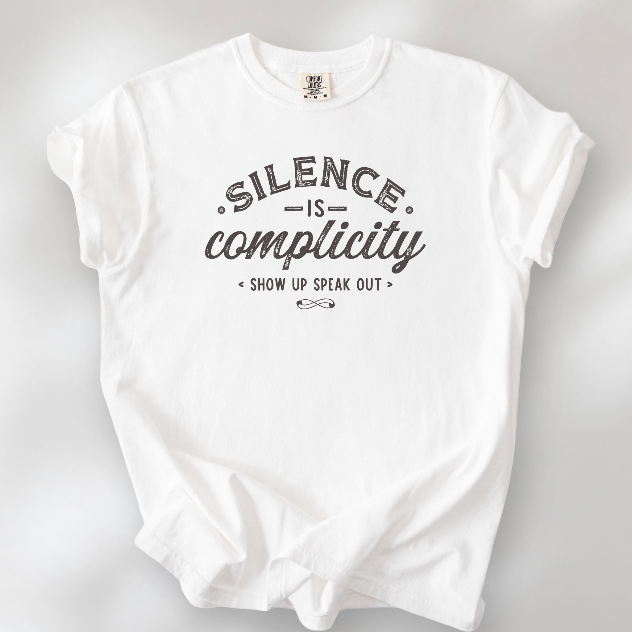 White t-shirt with vintage distressed typography reading “Silence Is Complicity – Show Up Speak Out.”