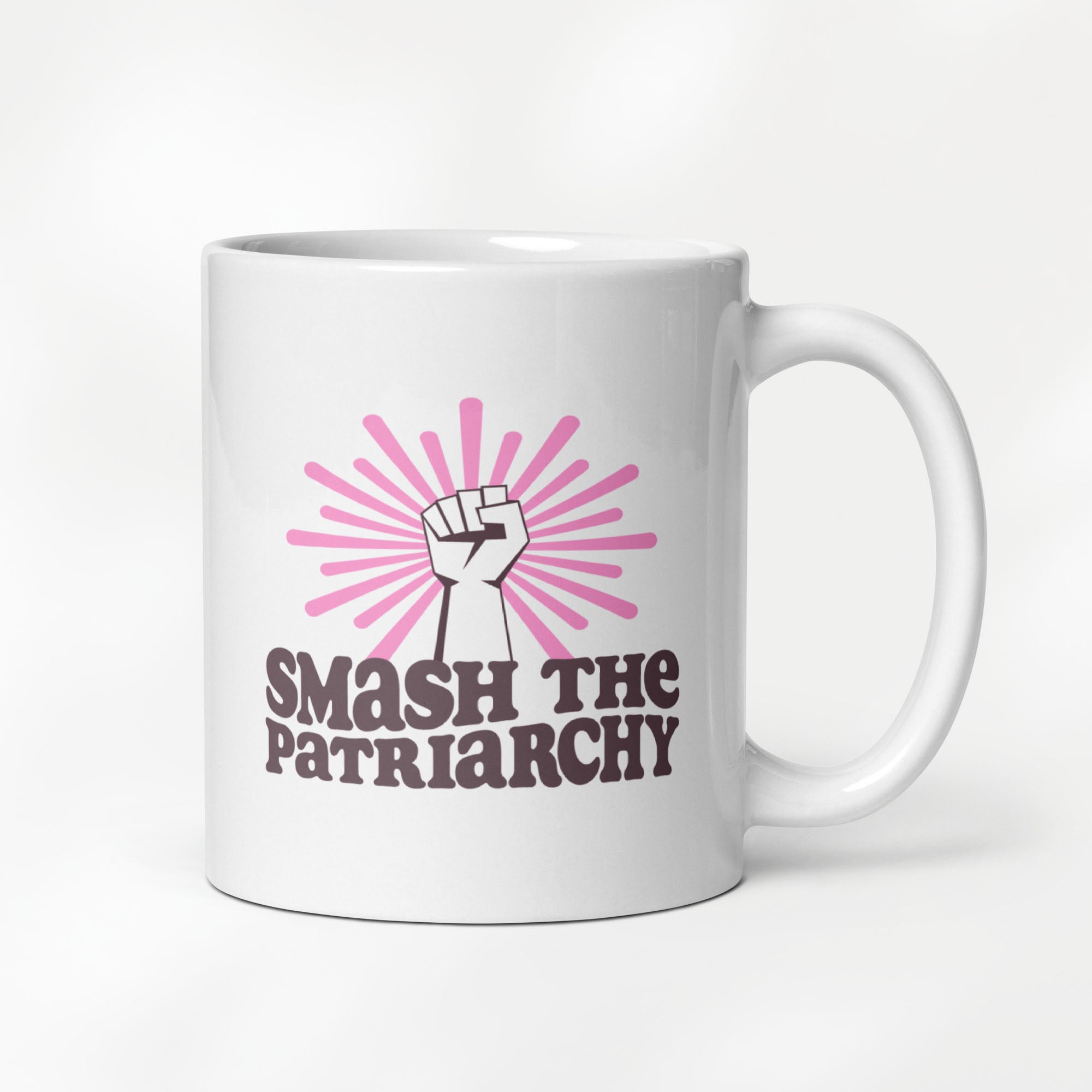 11 ounce ceramic mug that says "smash the patriarchy" below a raised fist centered in front of pink rays.