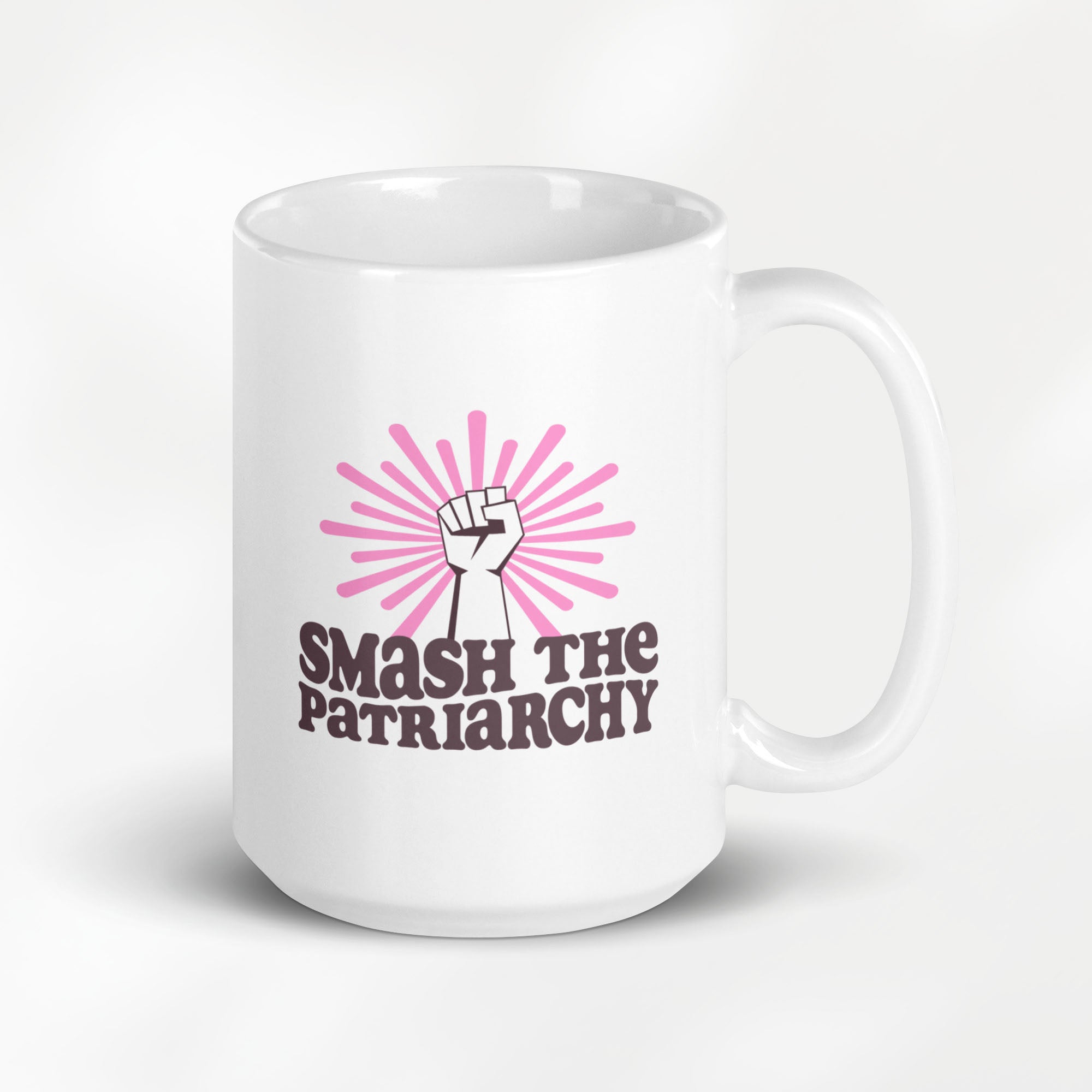 15 ounce ceramic mug that says "smash the patriarchy" below a raised fist centered in front of pink rays.